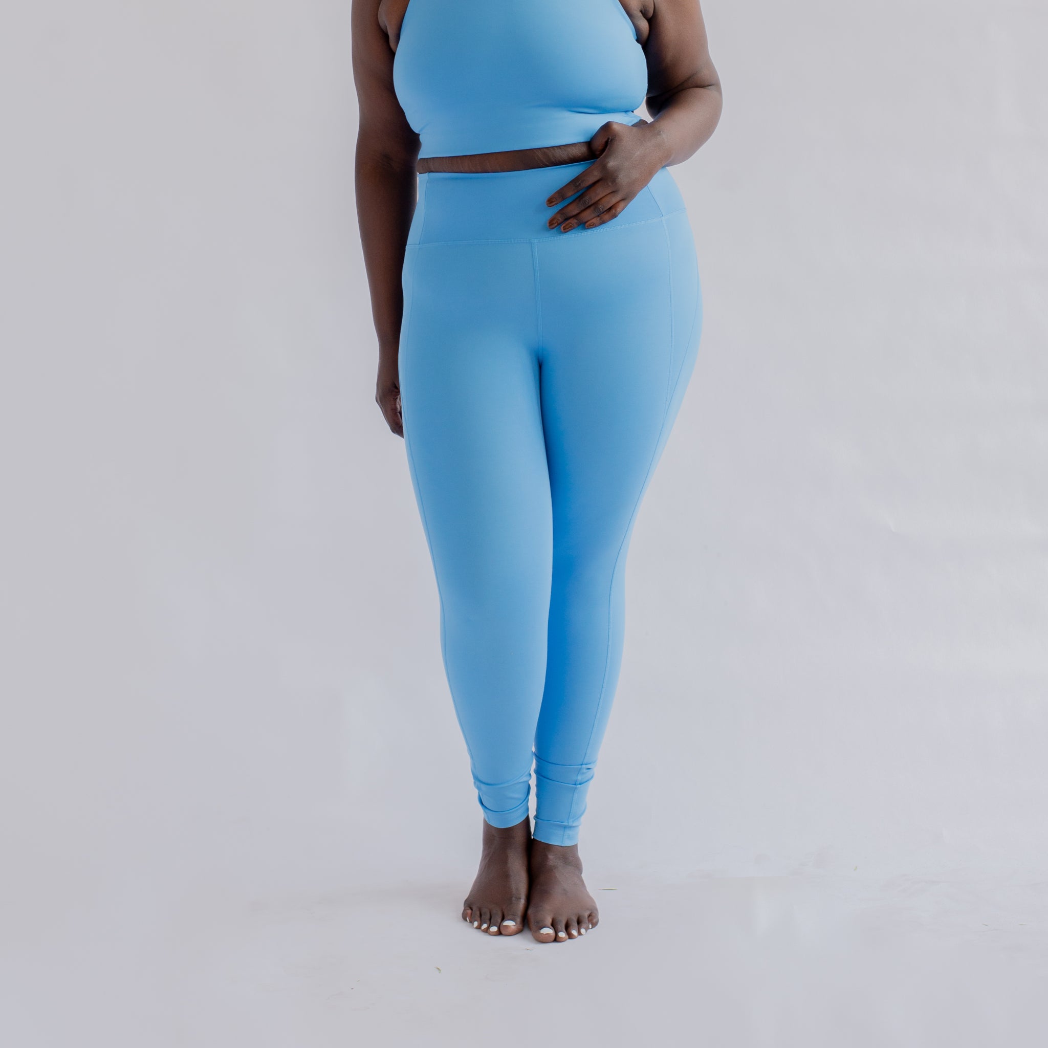 Person in hellblauem Sport-Outfit steht barfuß vor einem weißen Hintergrund.