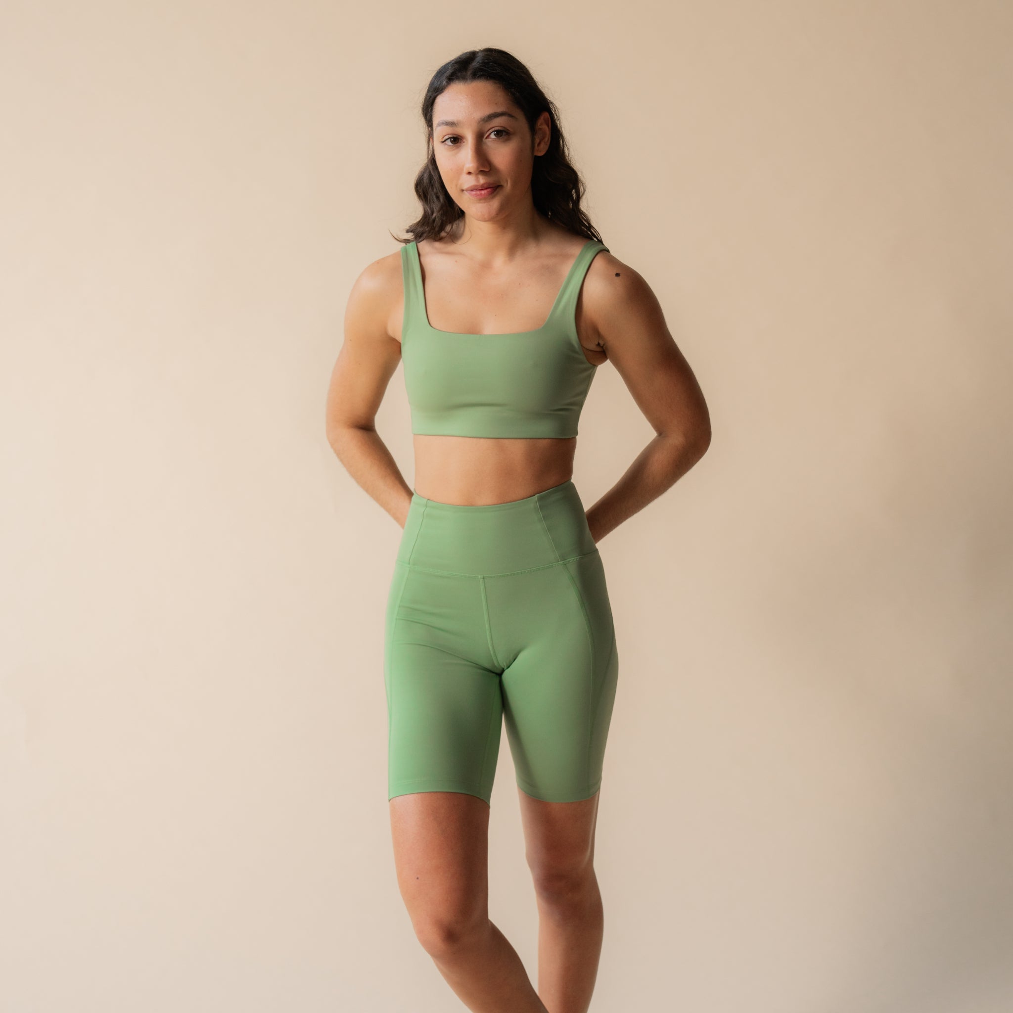 Eine Person in grüner Sportkleidung steht vor einem beigen Hintergrund.