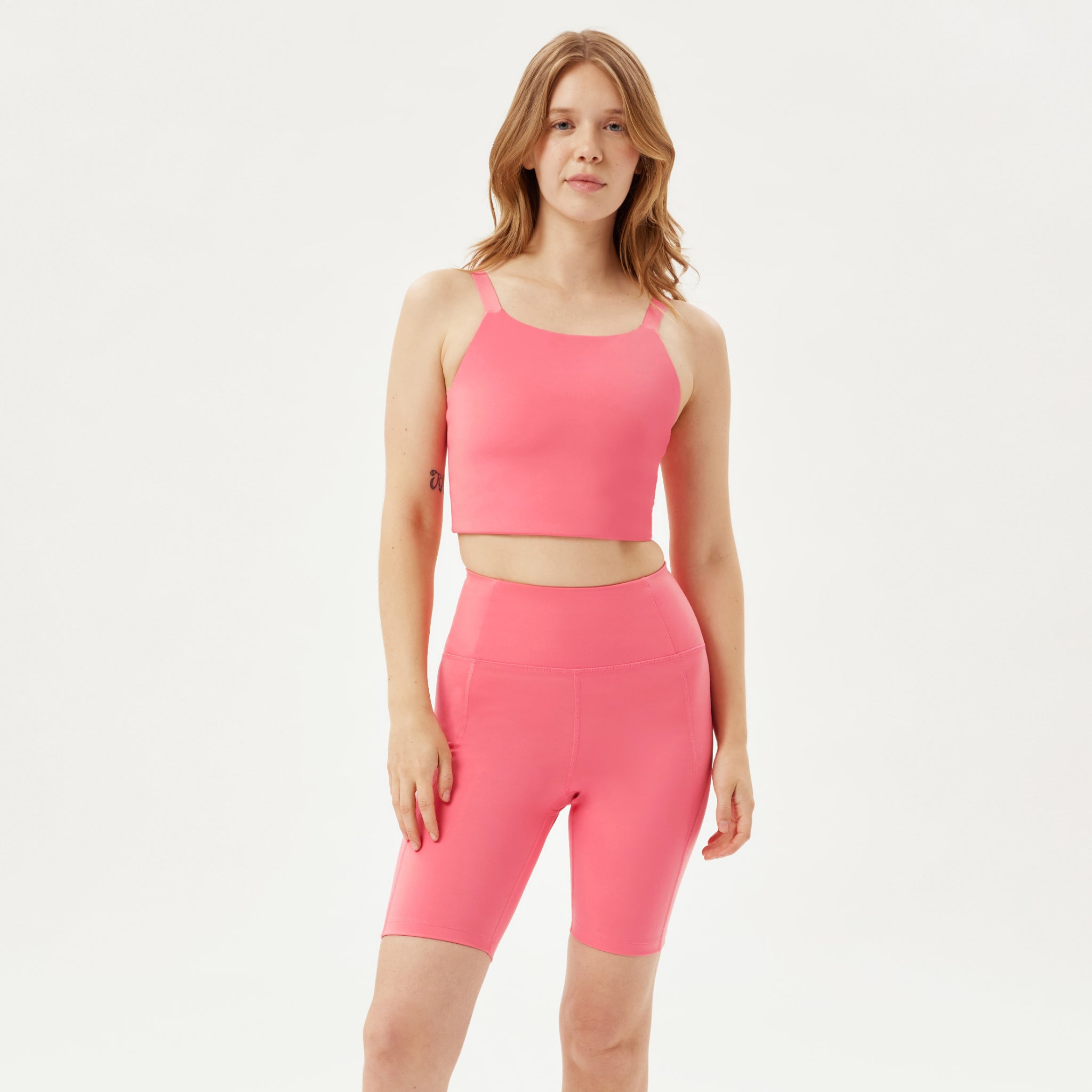 Frau in pinkem Sport-Set, bestehend aus einem ärmellosen Crop-Top und passenden Shorts, vor weißem Hintergrund.