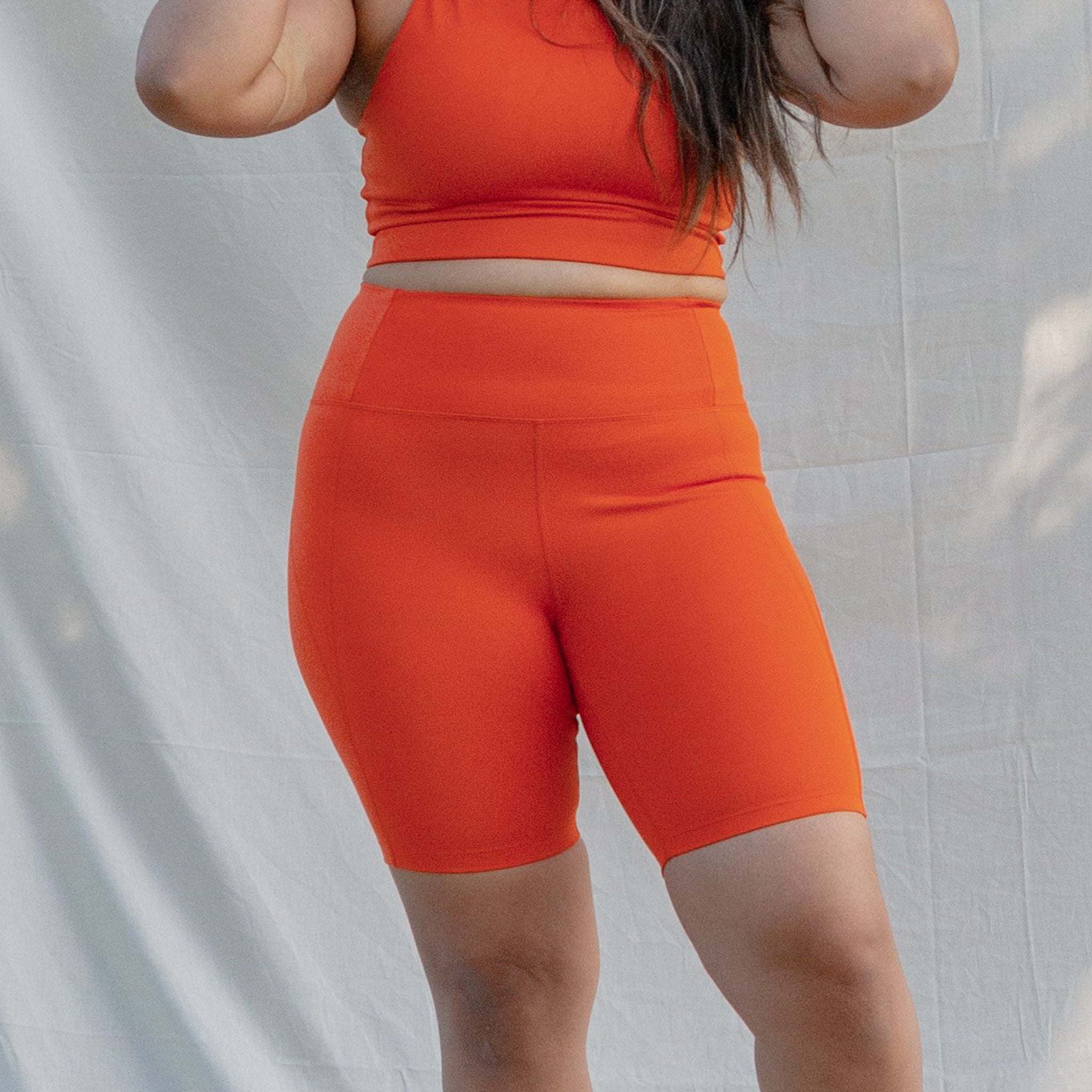 Eine Person trägt ein orangefarbenes Sportoutfit vor einem hellen Hintergrund.