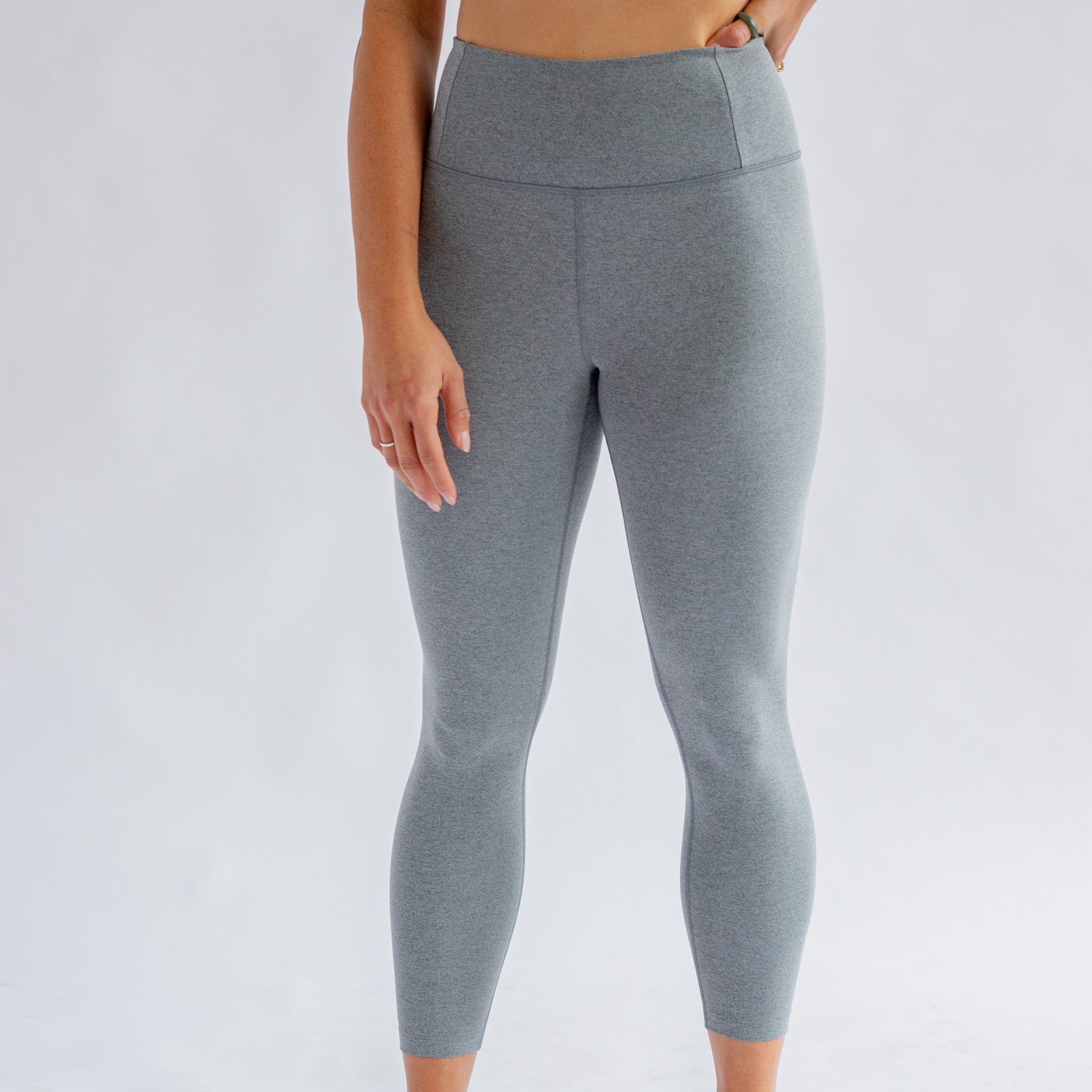 Person trägt graue Leggings vor einem hellen Hintergrund.