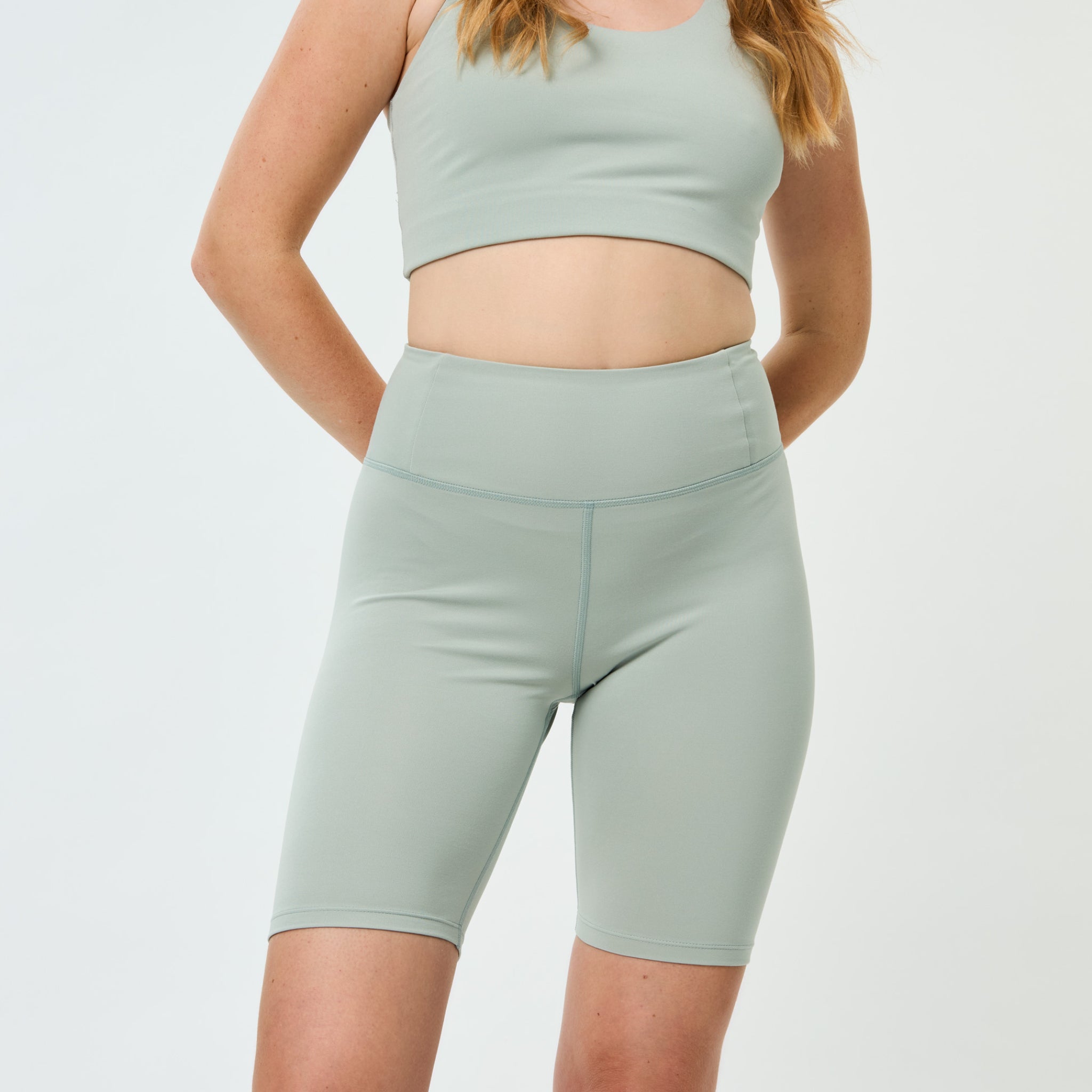 Frau in einem mintgrünen Sportset mit einem Top und Shorts, aufgenommen vor einem weißen Hintergrund.