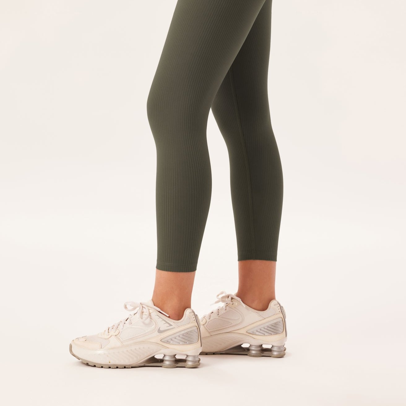 Person trägt olivgrüne Leggings und weiße Turnschuhe auf hellem Hintergrund.