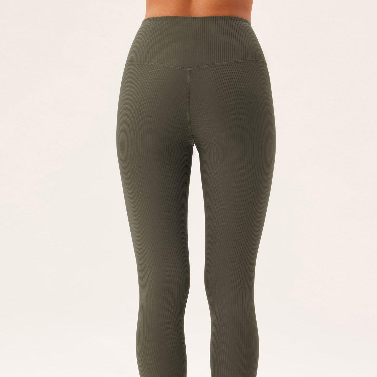 Eine Person trägt eng anliegende, olivgrüne Leggings mit gerippter Struktur, fotografiert von hinten vor weißem Hintergrund.