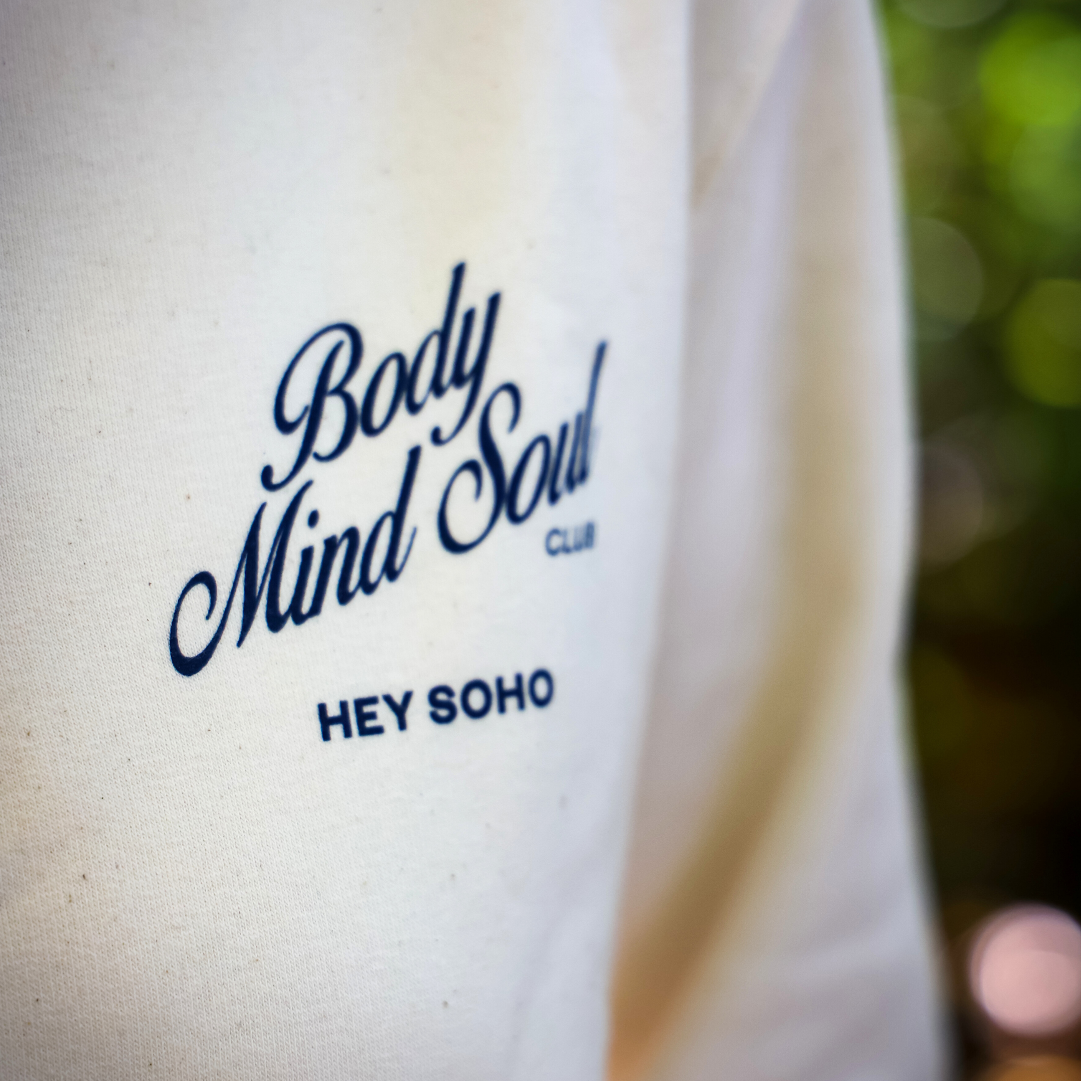 Nahaufnahme eines beigen Stoffes mit dem blauen Aufdruck "Body Mind Soul Club" und "Hey Soho".