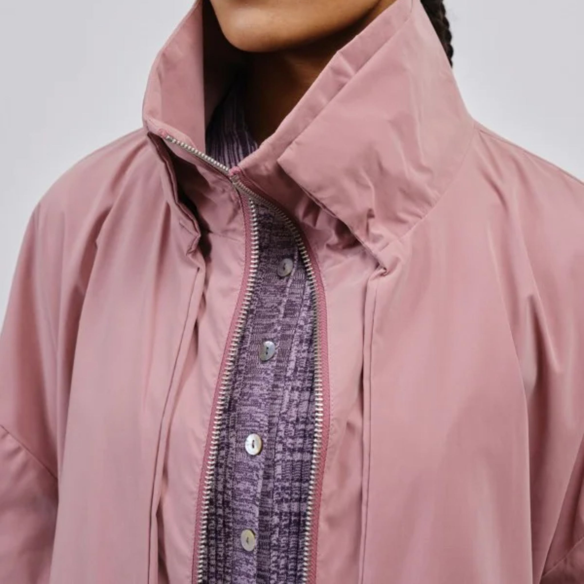 Eine Person trägt eine rosa Jacke mit Stehkragen über einem lila Hemd.