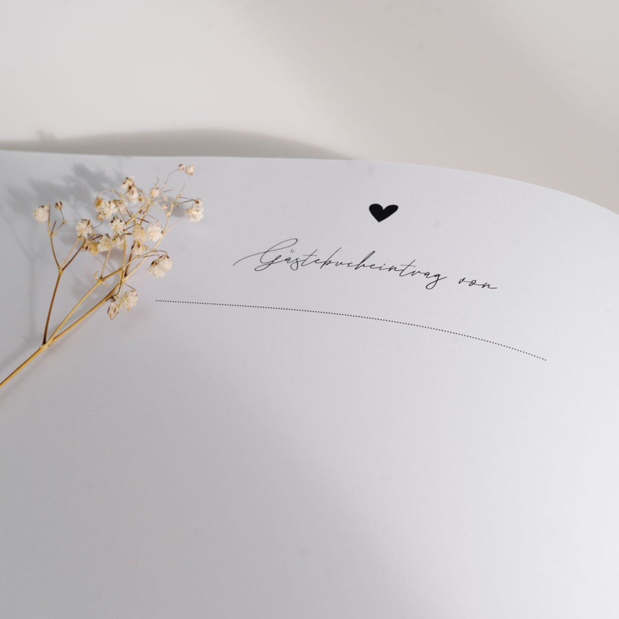 Seite eines Gästebuchs mit der Aufschrift "Gästebucheintrag von" und einem kleinen Herzsymbol, daneben Trockenblumen.