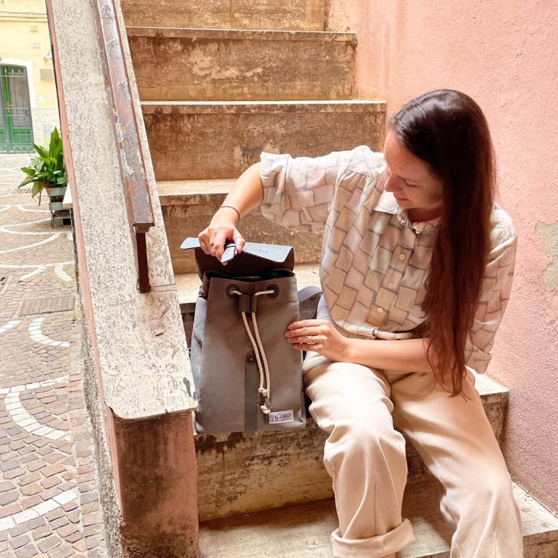 Eine Frau sitzt auf einer Treppe und packt Gegenstände aus einem grauen Rucksack aus.