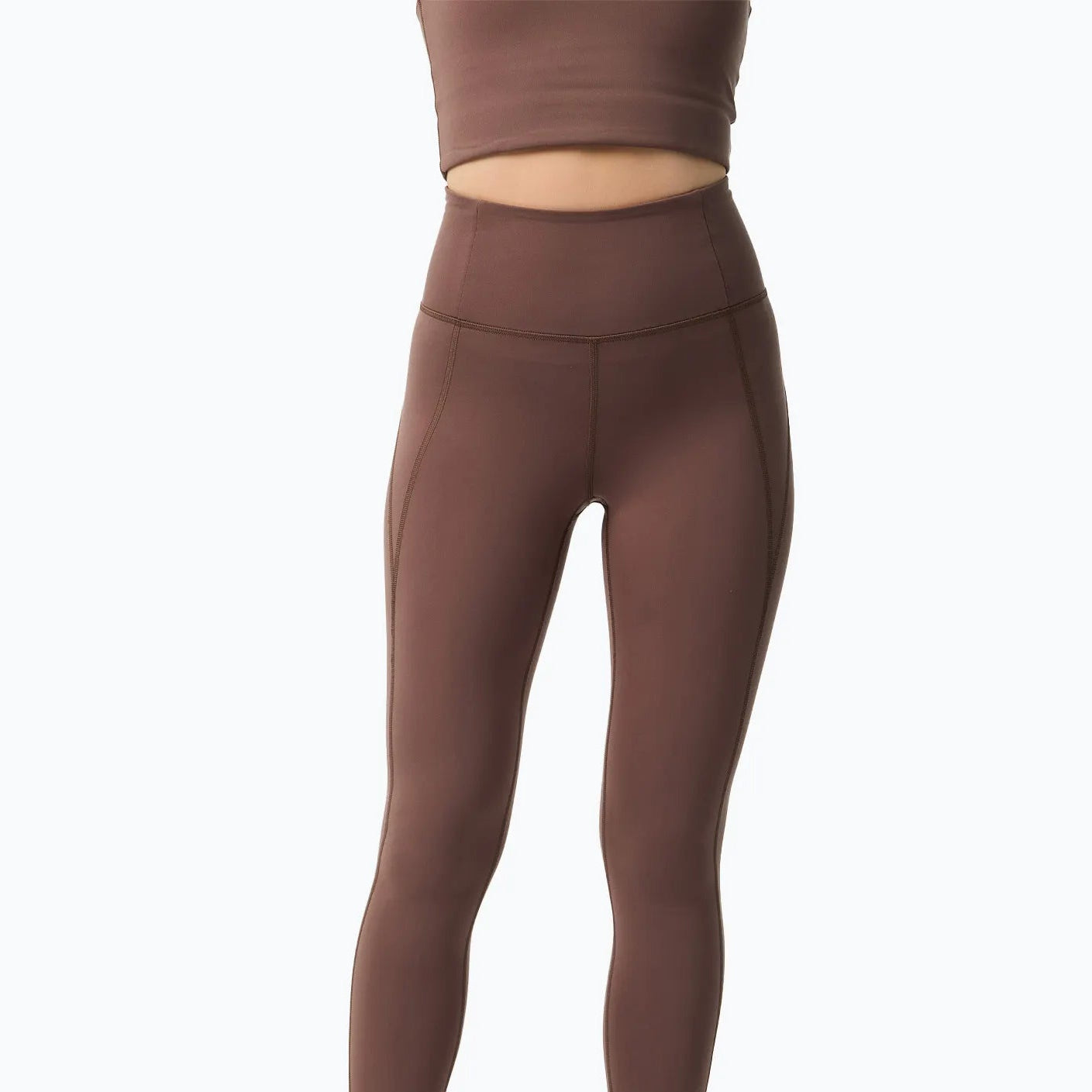 Eine Person, die ein braunes, ärmelloses Crop-Top und dazu passende Leggings mit hoher Taille trägt, wird von den Schultern abwärts vor einem schlichten weißen Hintergrund gezeigt.