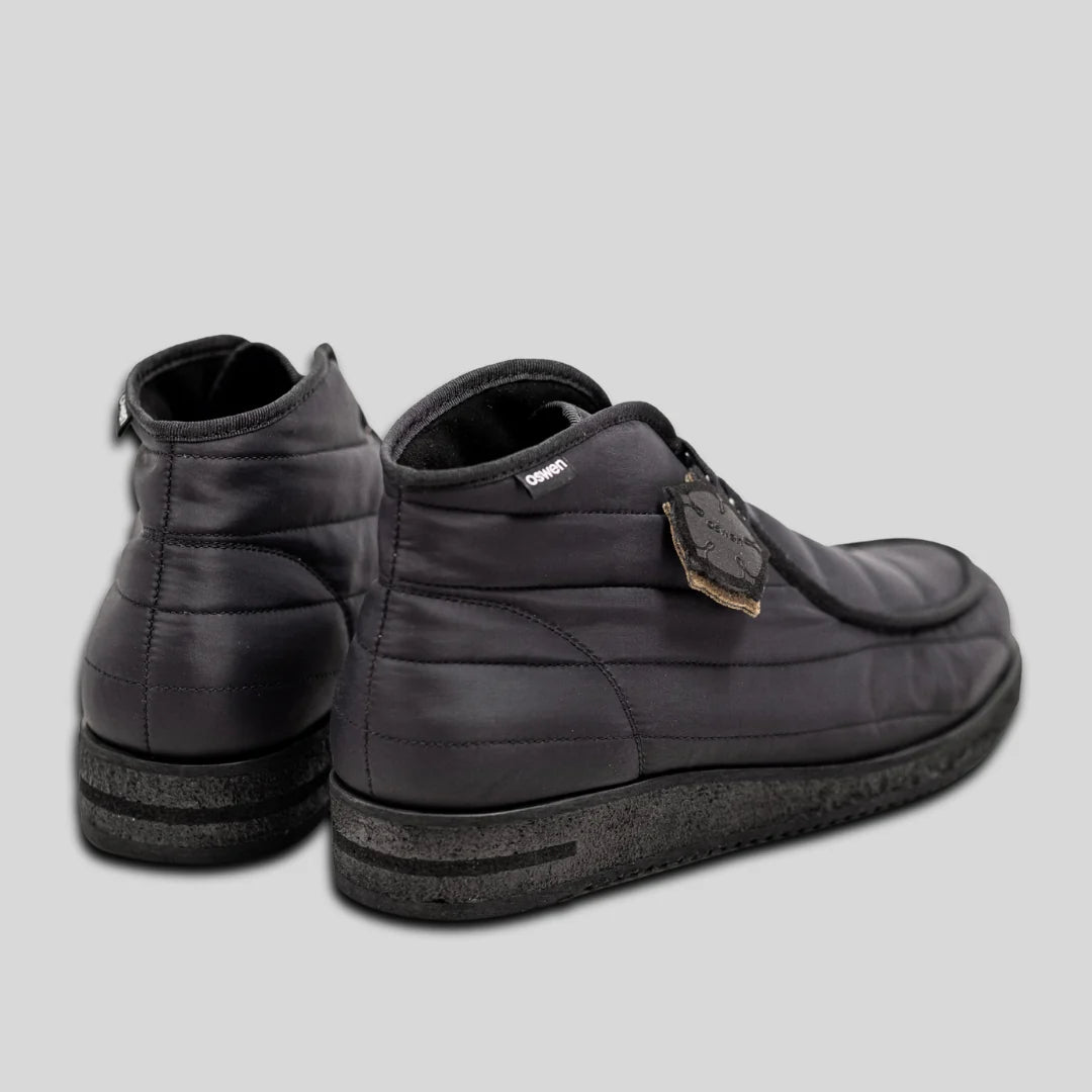 Ein Paar dunkelgraue, gepolsterte High-Top-Sneakers mit strukturierten schwarzen Sohlen, von hinten und von der Seite gesehen, auf hellgrauem Hintergrund. Ein Schuh hat ein Etikett in der Nähe der Schnürsenkel befestigt.