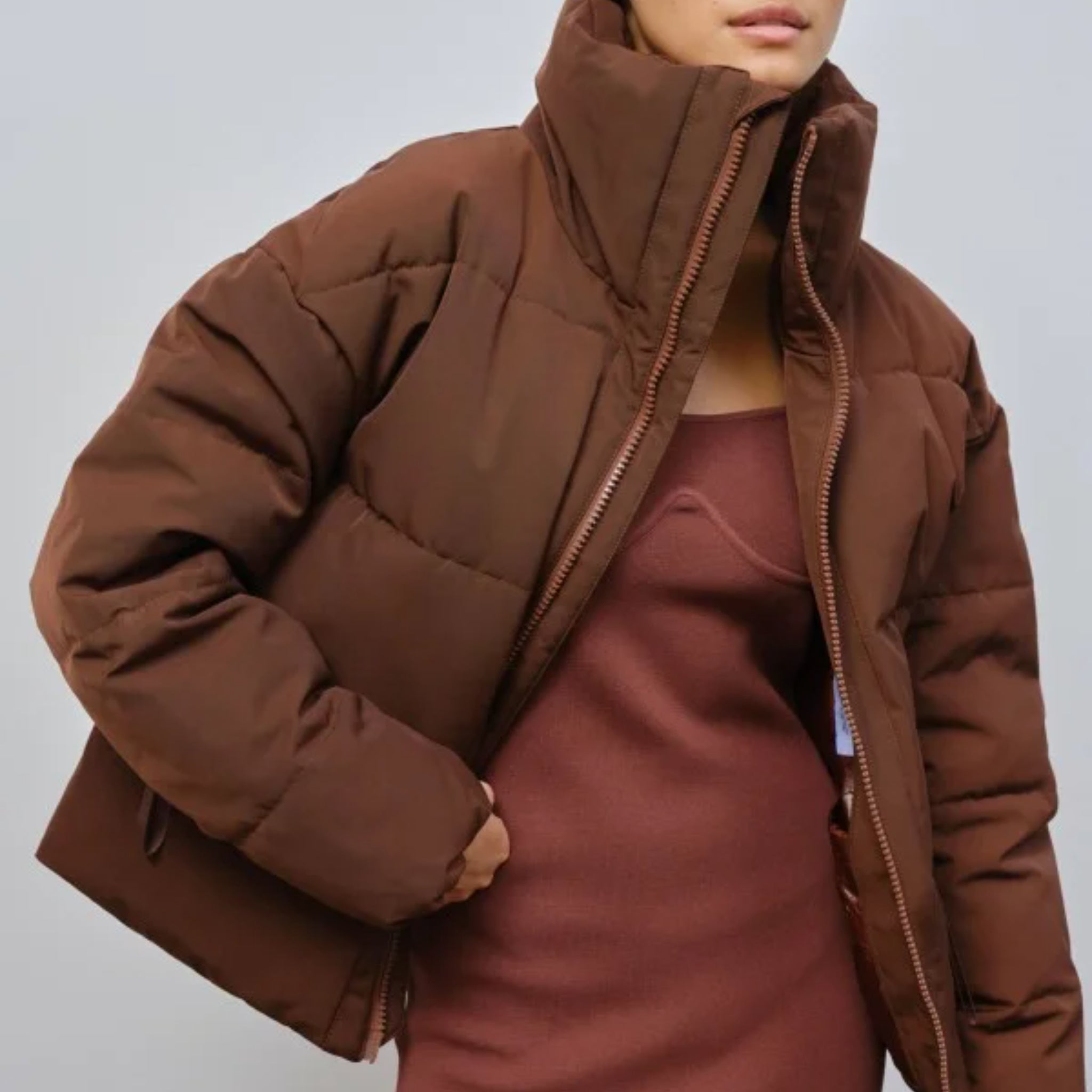 Person in a brauner Daunenjacke über einem passenden Kleid mit hohem Kragen.