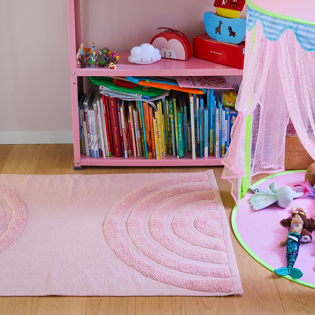 Rosa Kinderzimmer mit Bücherregal, Spielzeug und Teppich neben einem bunten Spielzelt mit Puppen auf dem Boden.