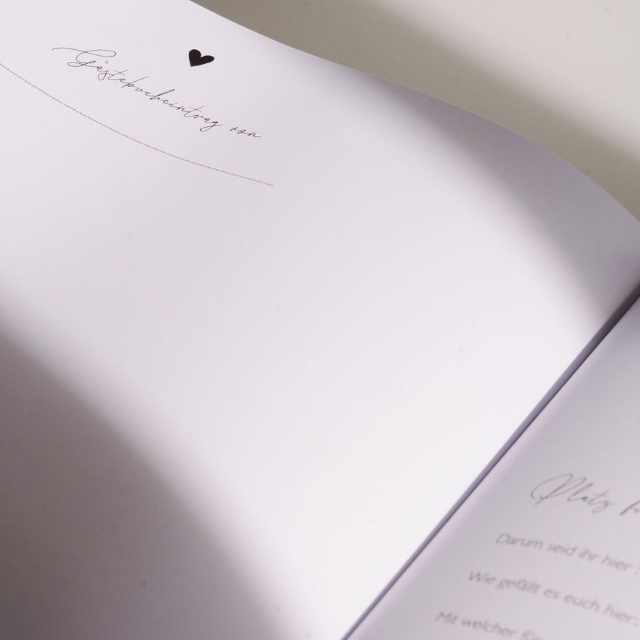 Offenes Buch mit einer herzförmigen Dekoration auf der Seite und teilweise sichtbarem handgeschriebenem Text.