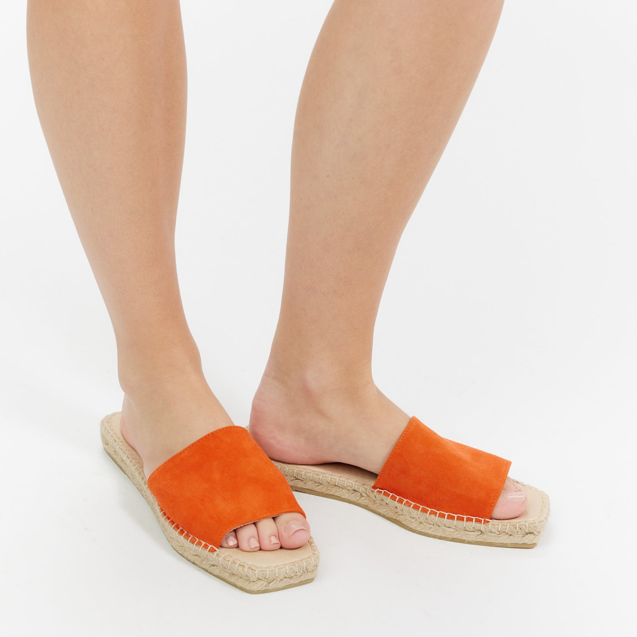 Beine in orangefarbenen Sandalen auf einem hellen Hintergrund.