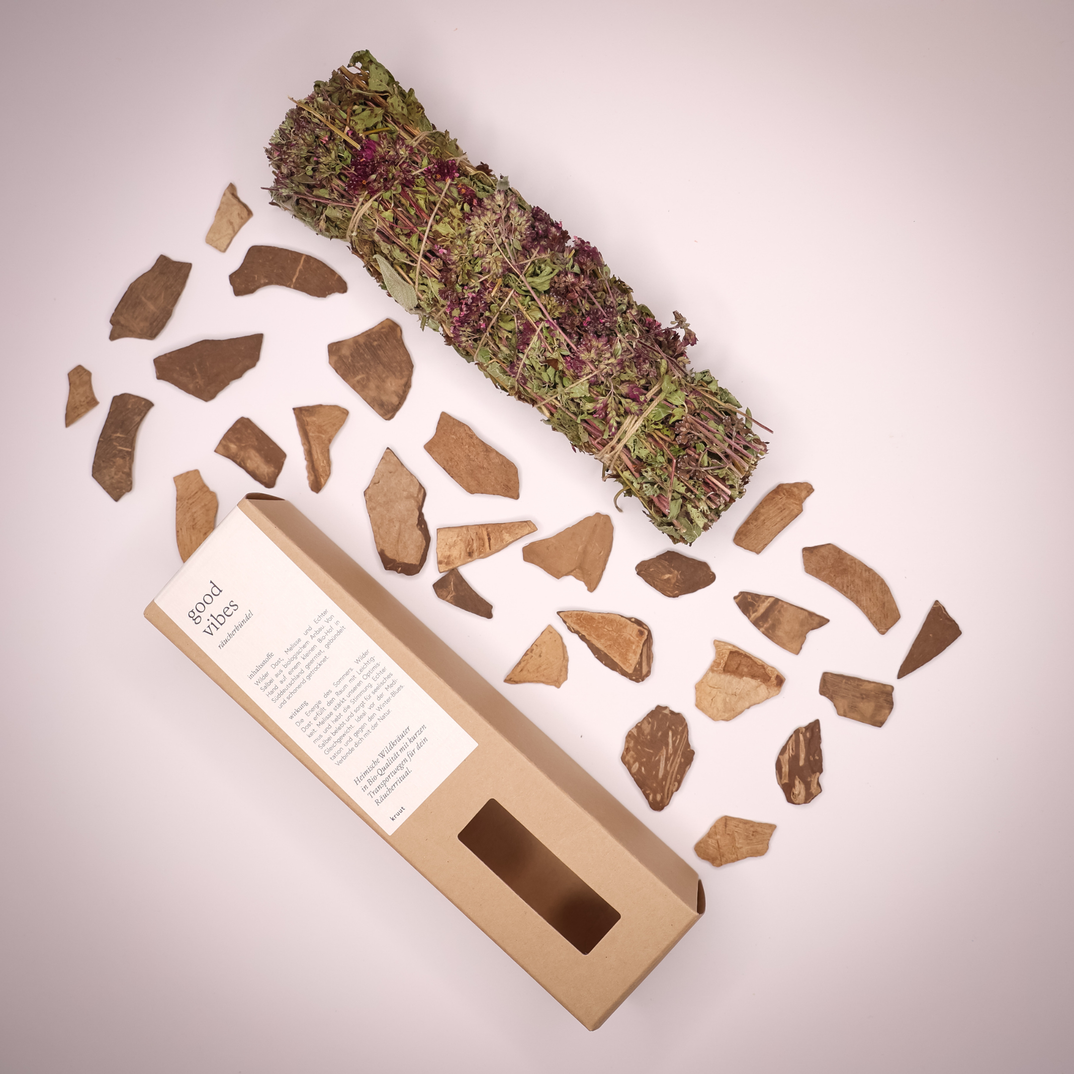 Ein Bündel getrockneter Kräuter mit Verpackung und verstreuten Holzstücken auf einem hellen Hintergrund.