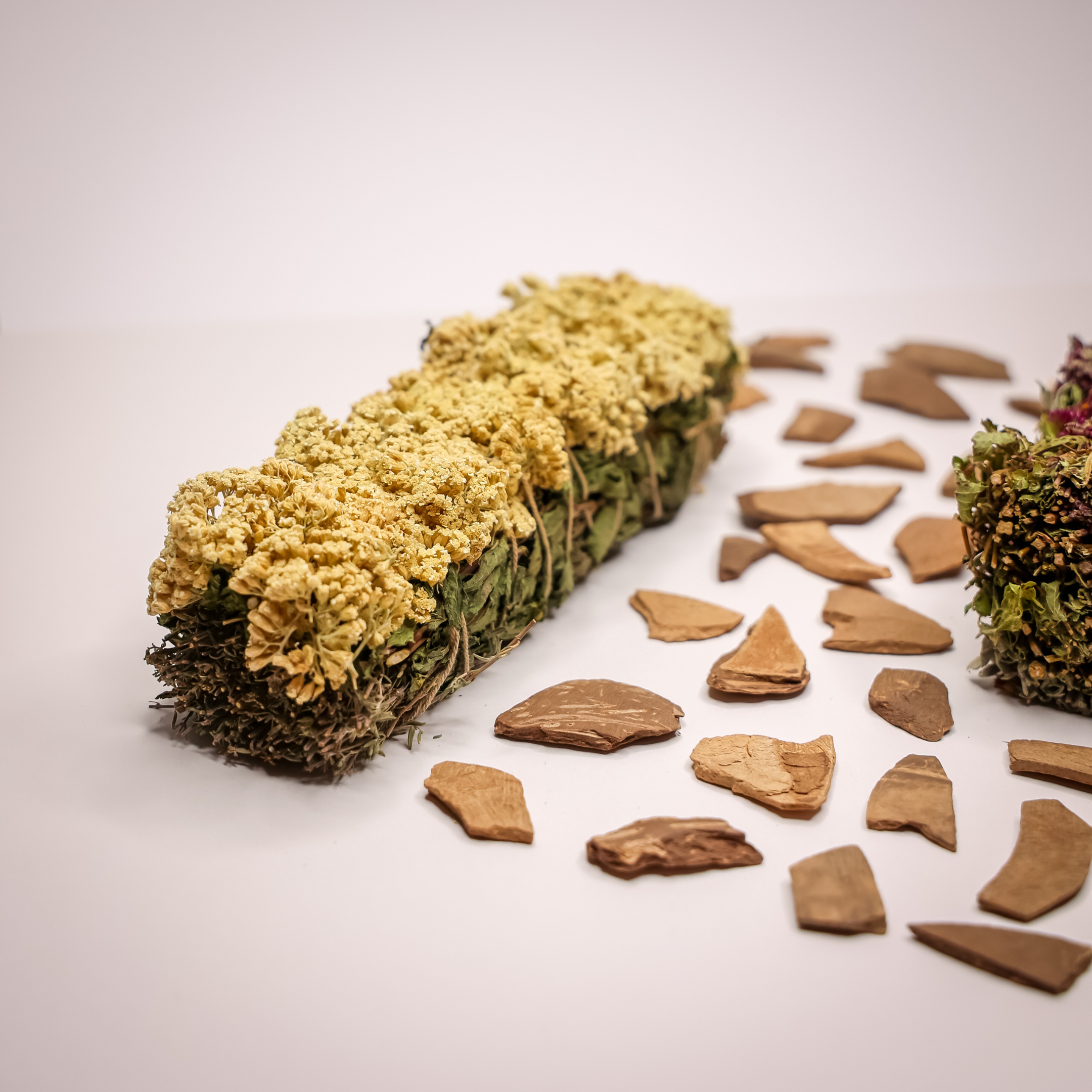 Ein Bündel aus gelben und grünen Trockenblumen liegt auf einem Tisch, umgeben von Holzstücken.