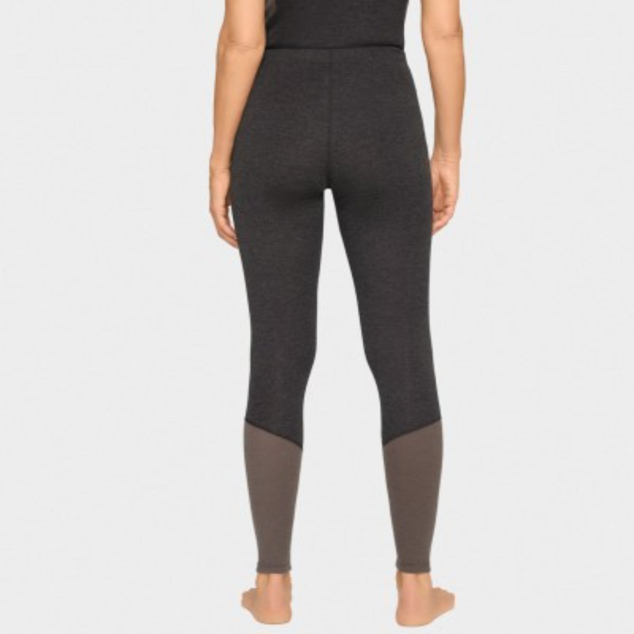 Eine Person steht barfuß, von hinten gesehen, und trägt hoch taillierte, taillierte Leggings, die dunkelgrau sind mit helleren grauen Einsätzen an den Unterschenkeln. Der Hintergrund ist einfarbig und hell gefärbt.