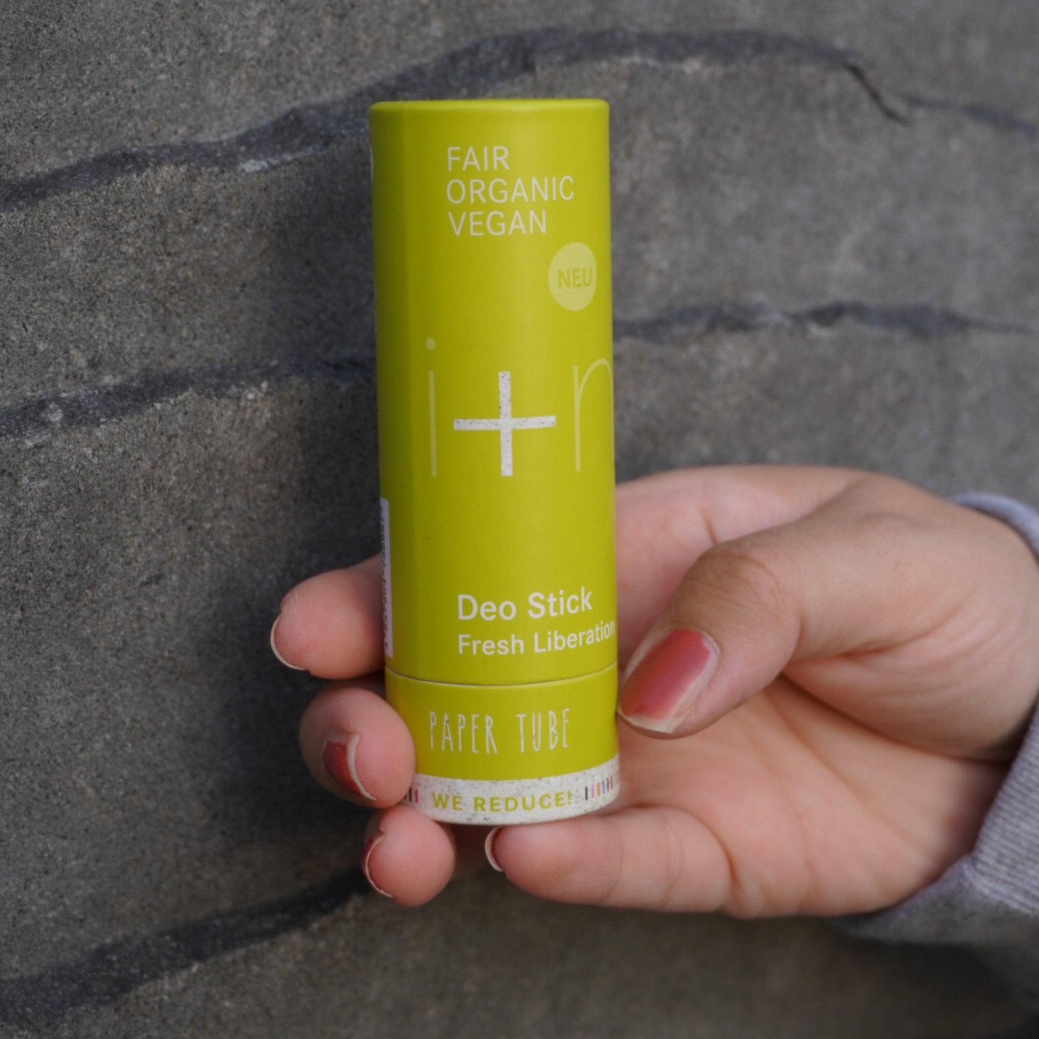 Hand hält einen grünen, fairen, organischen, veganen Deo-Stick vor einer grauen Wand.