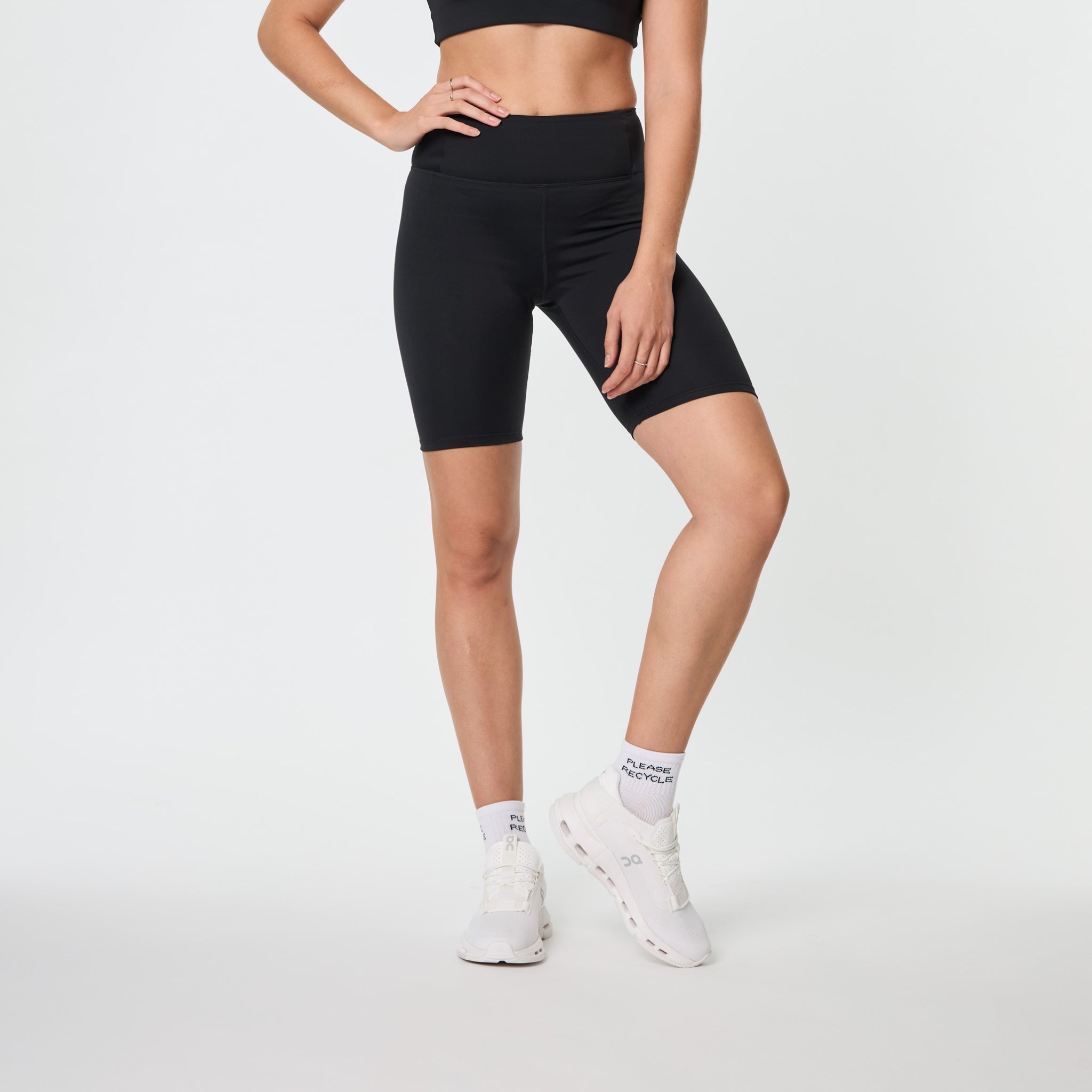 Person in schwarzem Sportoutfit und weißen Sneakers posiert vor weißem Hintergrund.