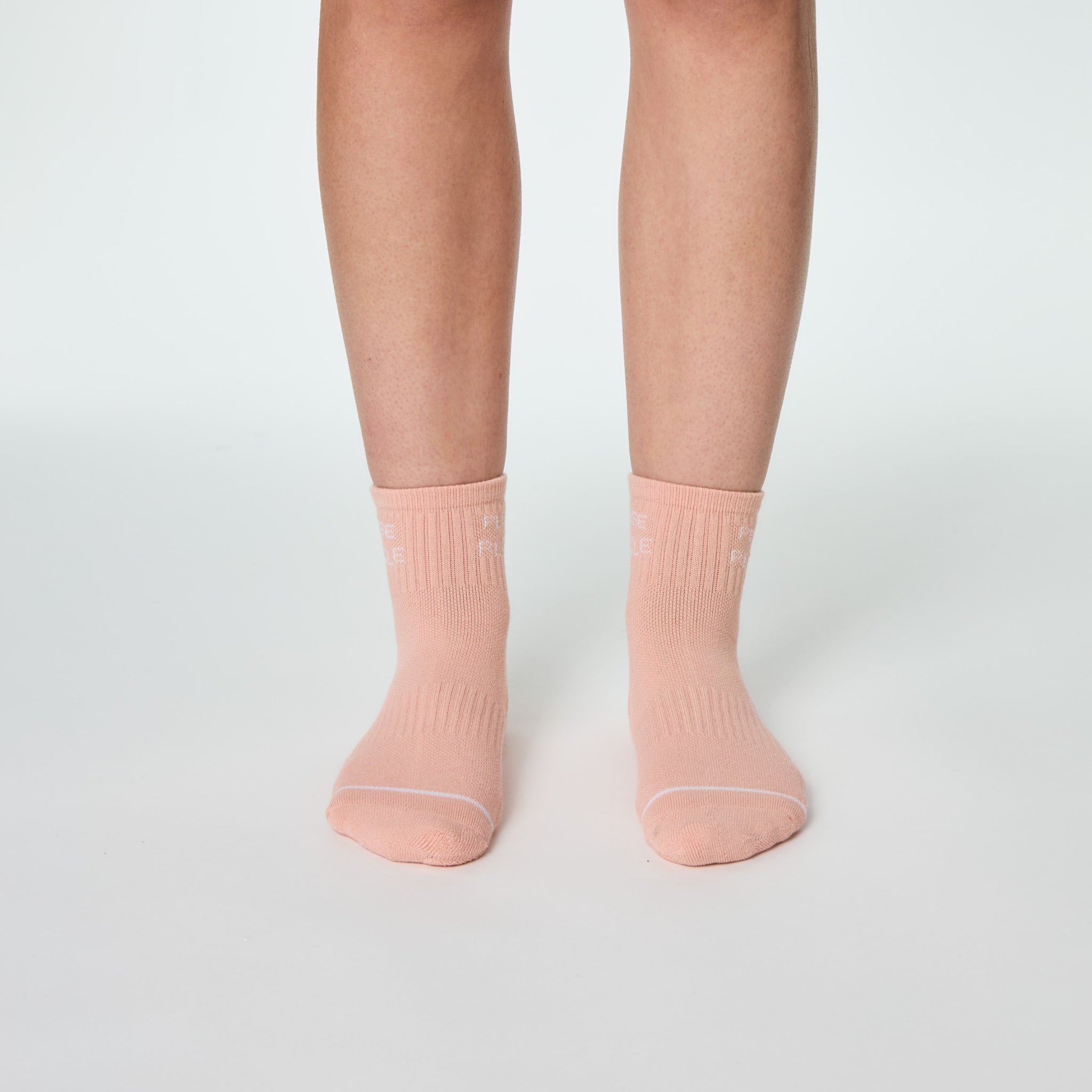 Beine in pfirsichfarbenen Socken auf weißem Hintergrund.