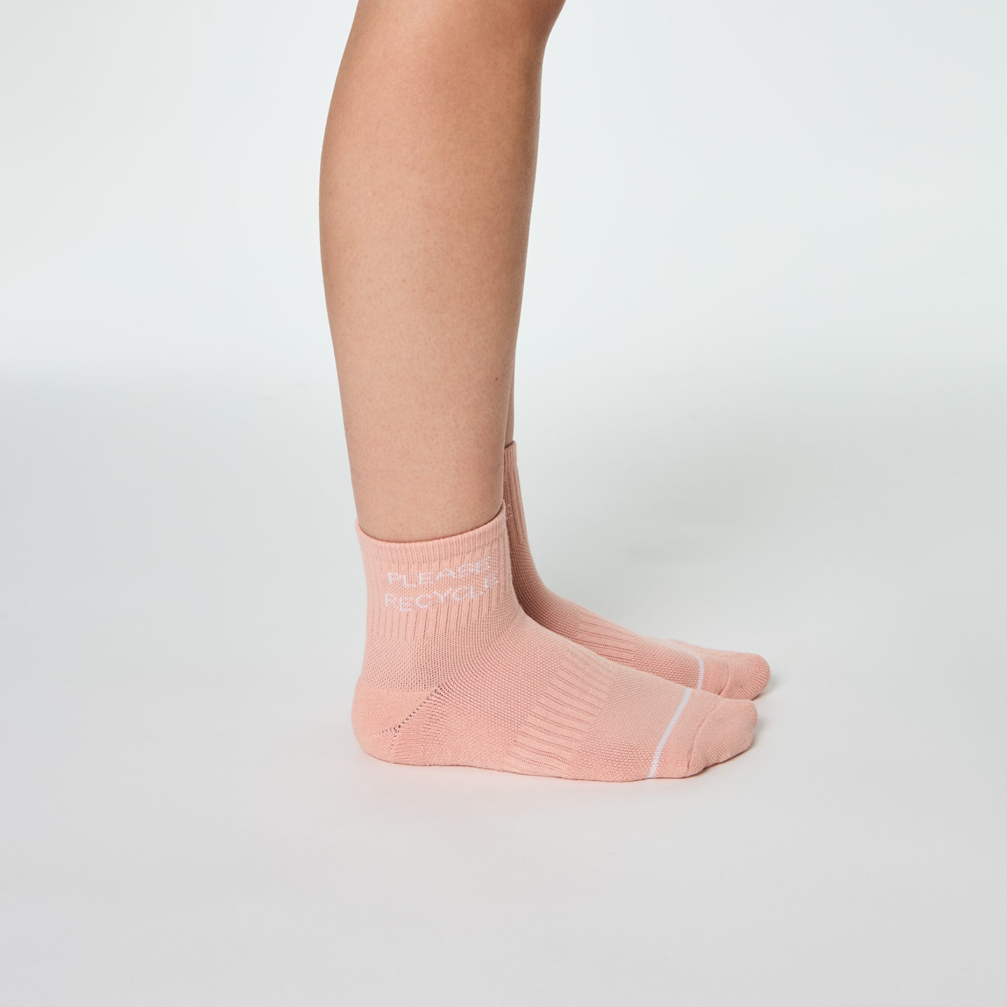Seitenansicht eines Beins, das einen rosa Socken mit der Aufschrift "Please Recycle" auf hellem Hintergrund trägt.