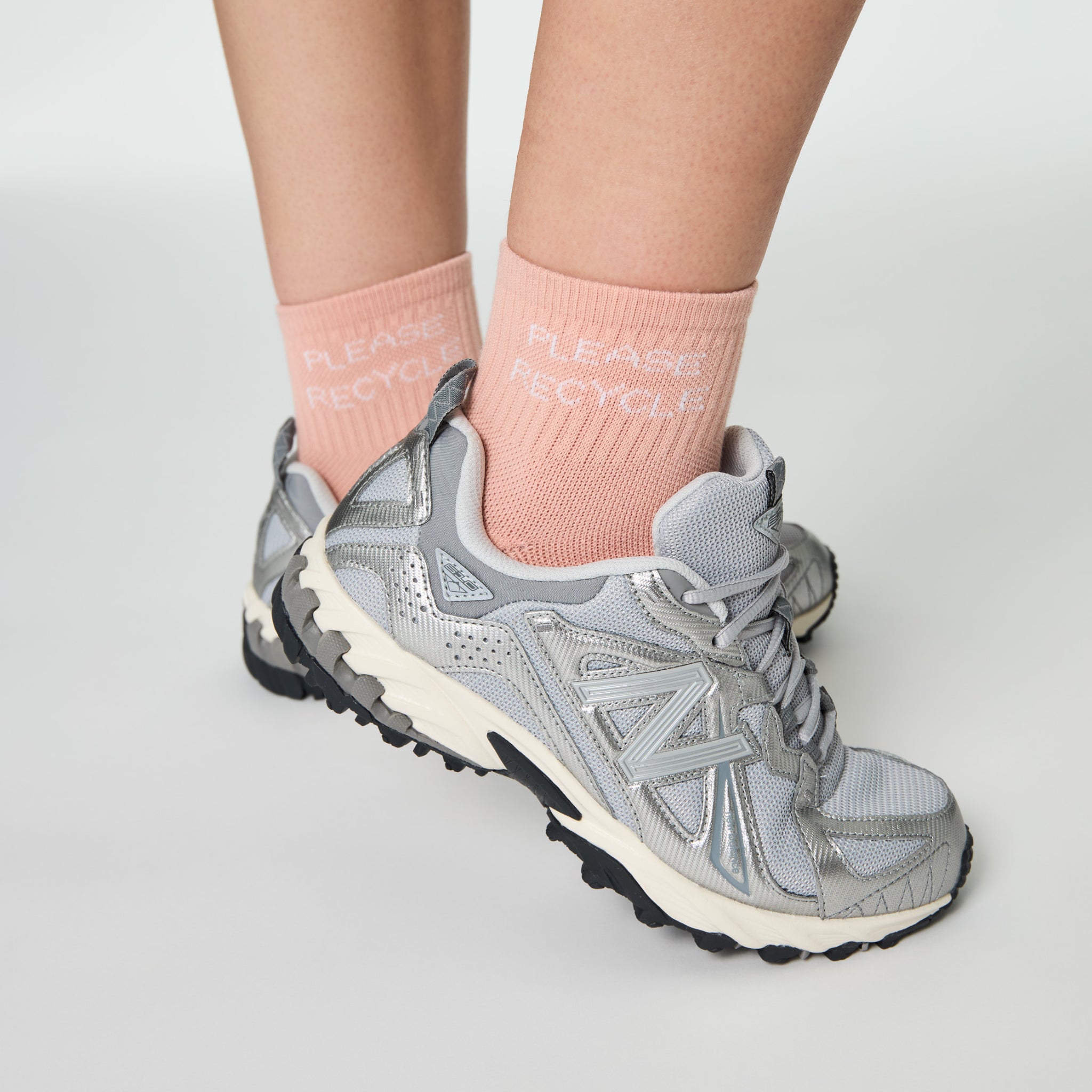 Nahaufnahme von grauen Sneakers und rosa Socken mit der Aufschrift "PLEASE RECYCLE".