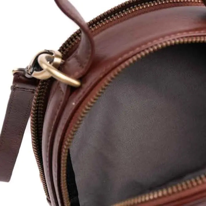 Nahaufnahme einer geöffneten braunen Ledertasche mit Reißverschluss, die das leere schwarze Stoffinnere und die Metallringe zur Befestigung der Griffe zeigt.