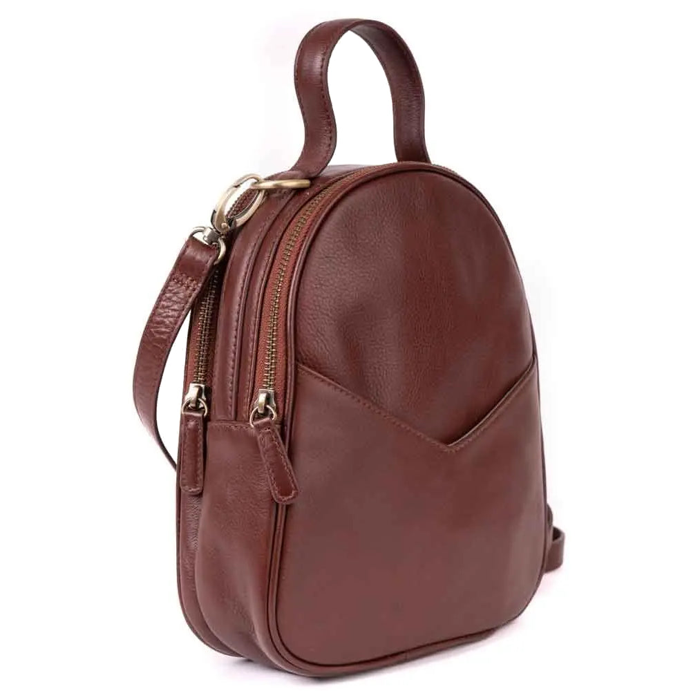 Kleiner brauner Lederrucksack mit Tragegriff, verstellbaren Schulterriemen, zwei goldenen Reißverschlüssen und einer Vordertasche. Die Tasche steht aufrecht auf einem weißen Hintergrund.
