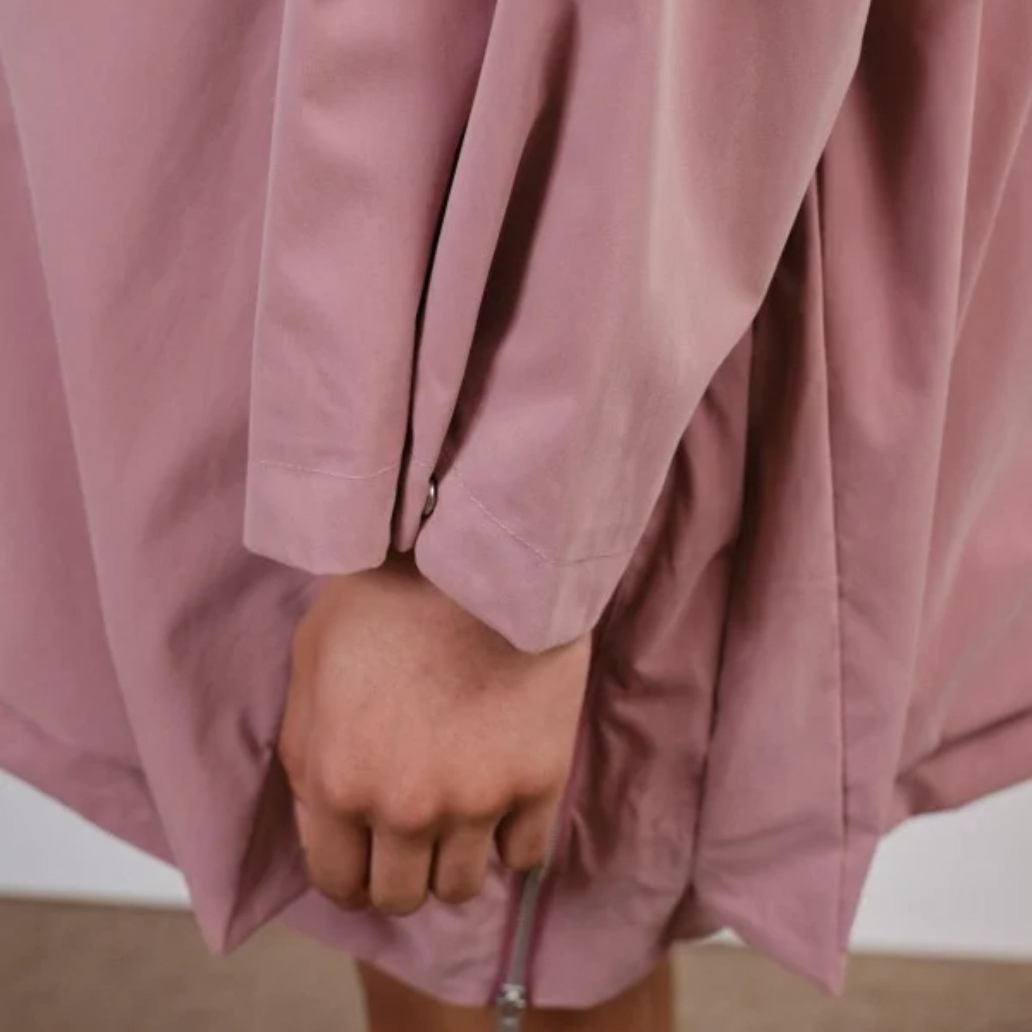 Eine Person trägt eine locker sitzende, rosafarbene Jacke, und die Hand ist sichtbar am Saum.