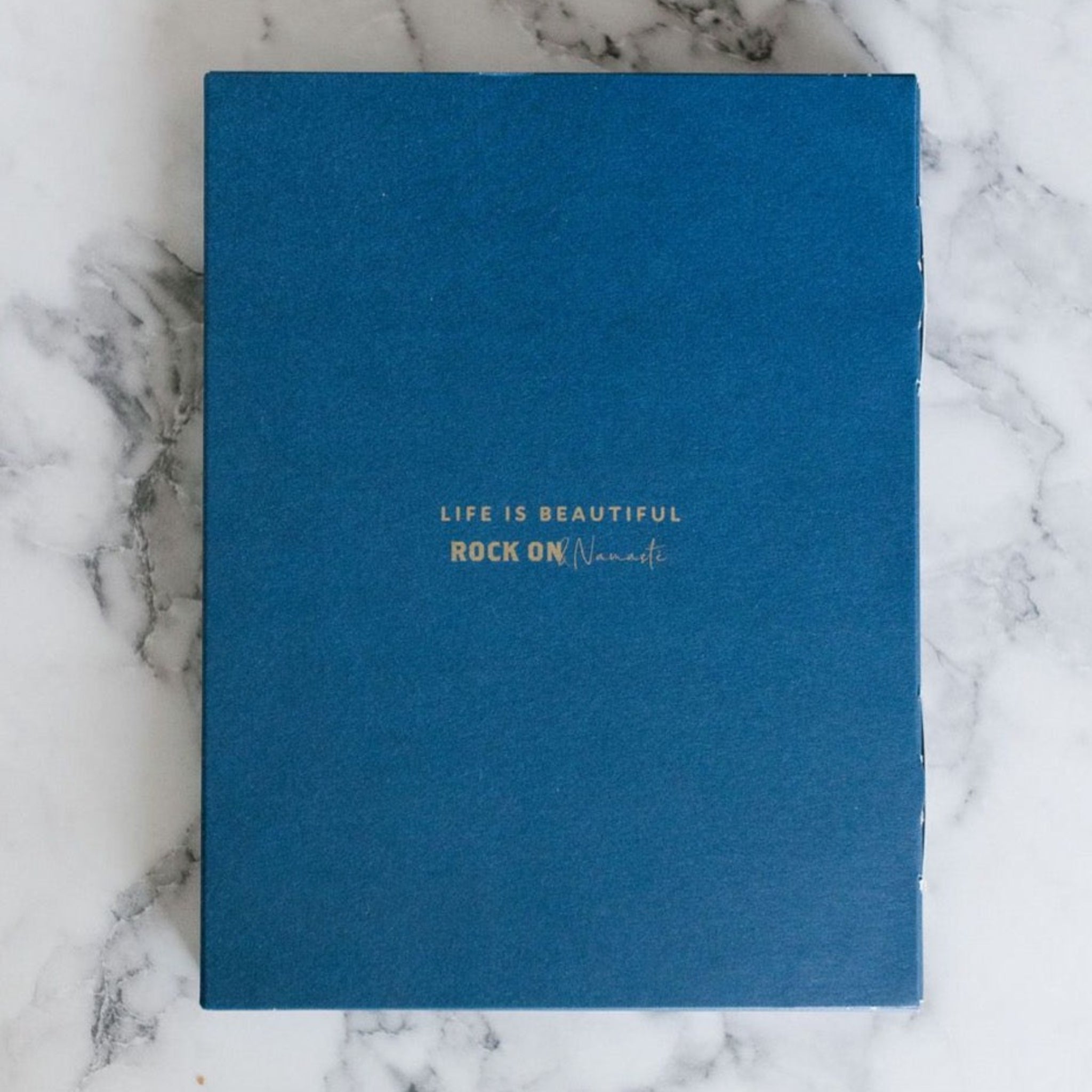 Blaues Buch auf Marmortisch mit Aufschrift: "Life is Beautiful - Rock On Namaste".