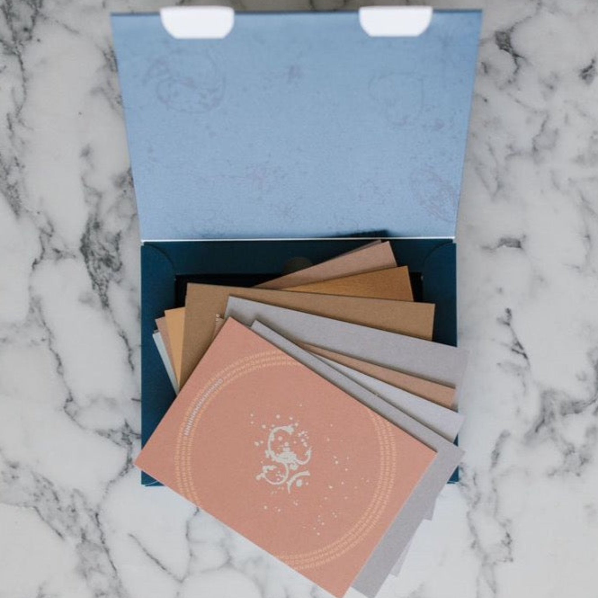 Eine offene blaue Box mit mehreren bunten Briefumschlägen liegt auf einer Marmoroberfläche.