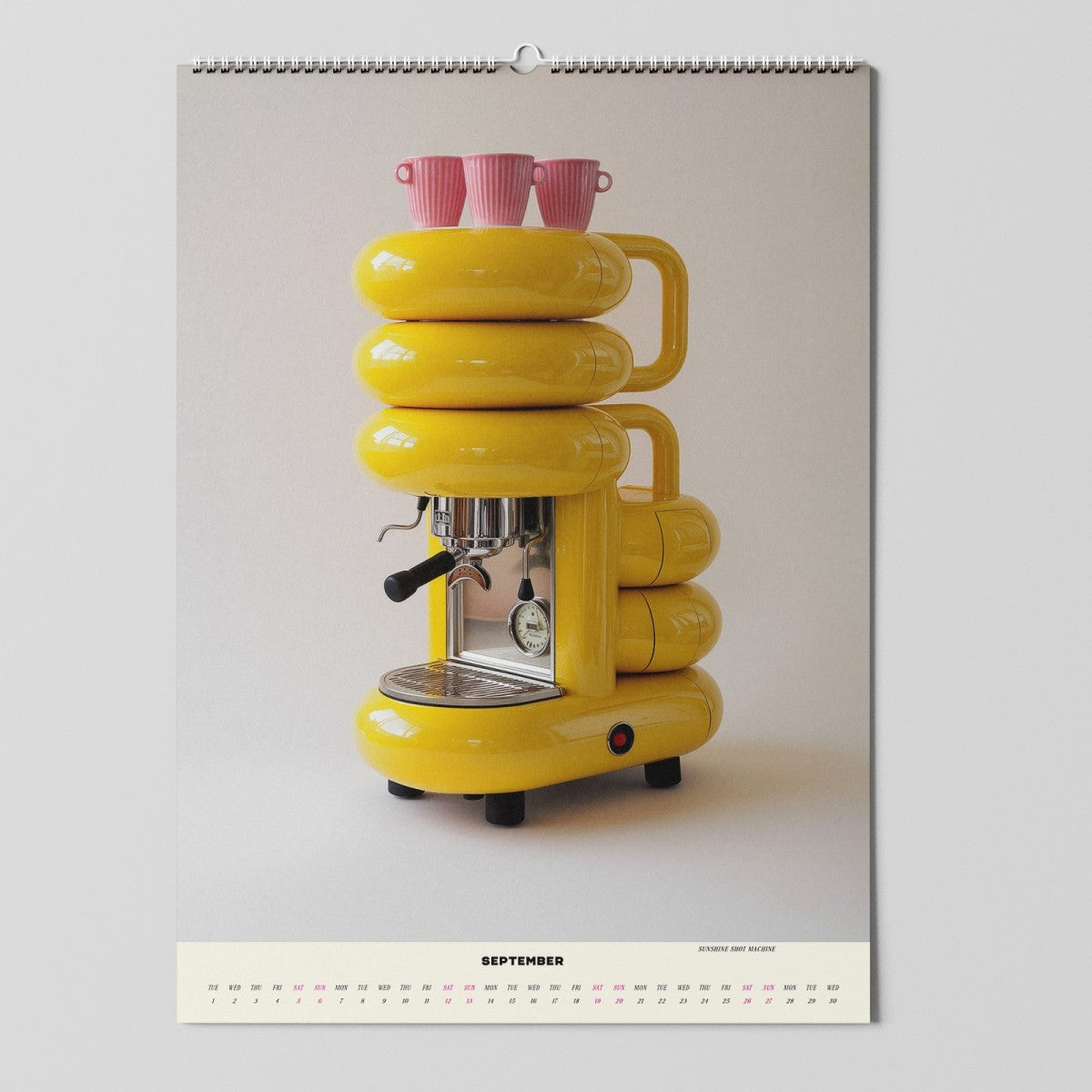 Ein Kalenderblatt für September zeigt eine gelbe Espressomaschine mit einem runden, modernen Design. Drei rosafarbene Tassen sitzen oben auf der Maschine und bilden einen Kontrast zu ihrer kräftigen Farbe.
