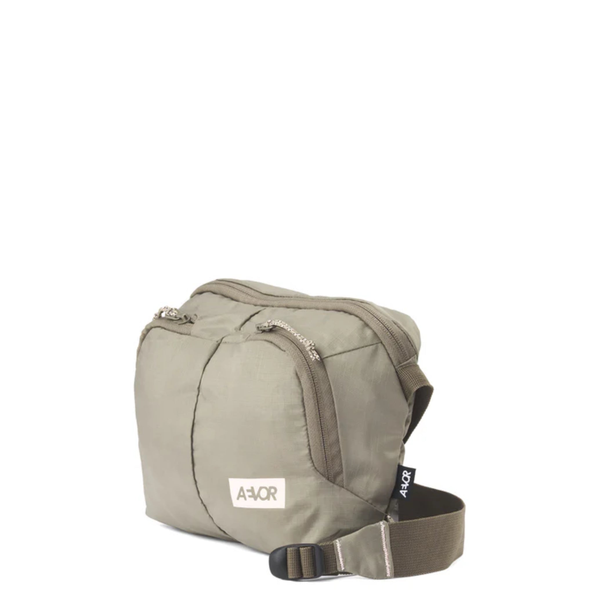 Eine kleine, hellolivgrüne Umhängetasche mit zwei Reißverschlussfächern, einem verstellbaren Riemen und einem weißen rechteckigen "AÁOR" Logoaufnäher auf der Vorderseite. Die Tasche ist auf einem schlichten weißen Hintergrund abgebildet.