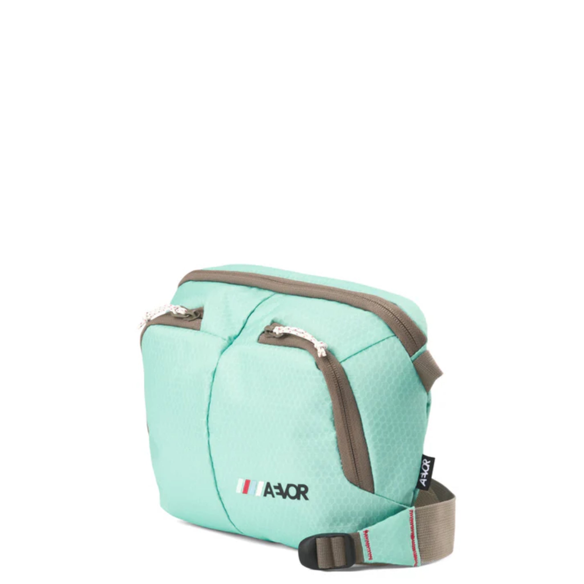 Eine kleine mintgrüne Crossbody-Tasche mit zwei Reißverschlusstaschen vorne, braunen Reißverschlüssen, einem verstellbaren Riemen und einem AEVOR-Logo mit kleinen vertikalen Streifen in Grün, Weiß und Rot.