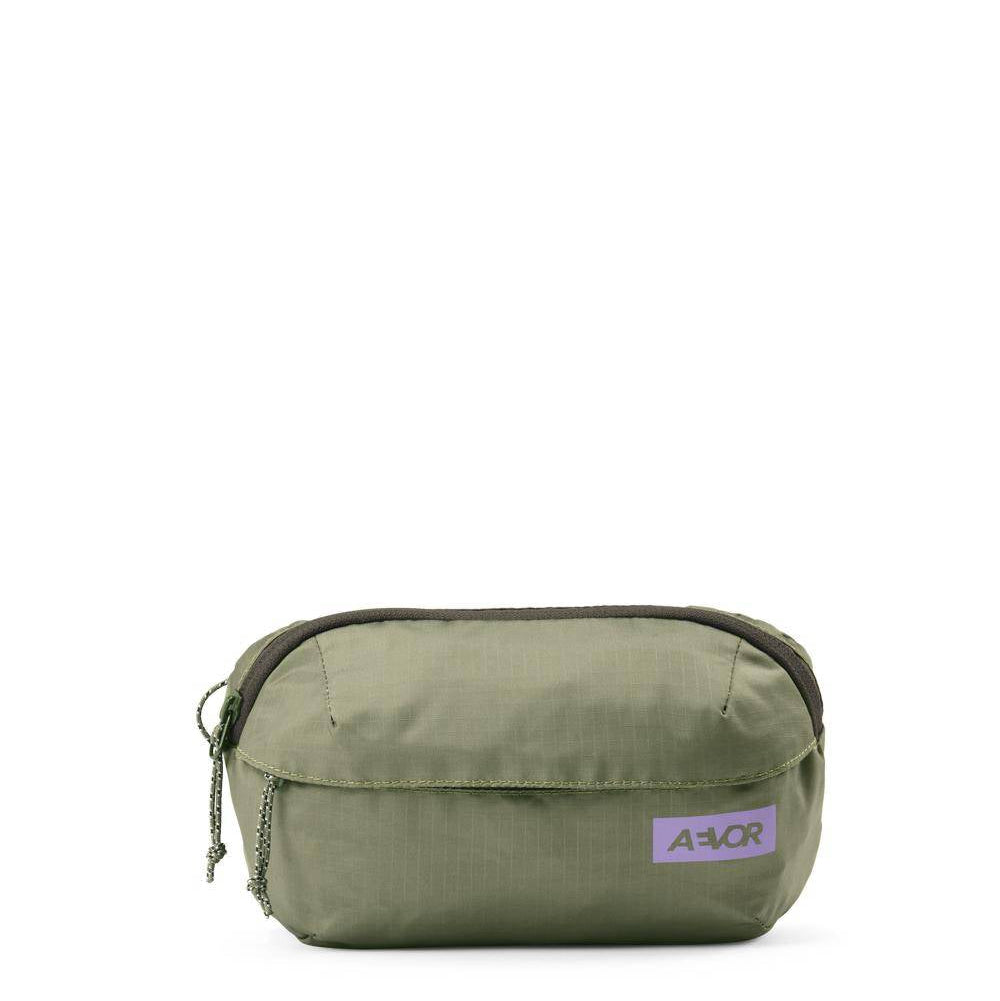 Eine kleine olivgrüne Reißverschlusstasche mit einer Vordertasche und einem lila AVOR-Logoaufnäher auf weißem Hintergrund.