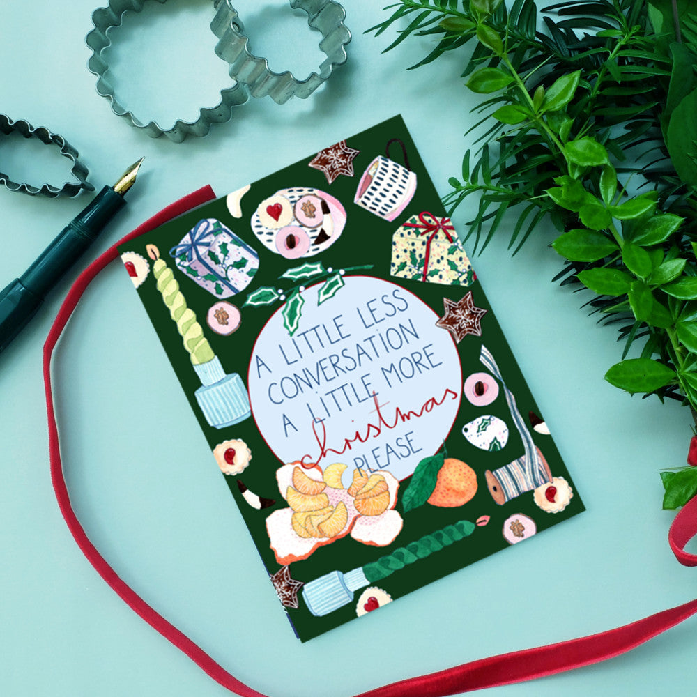 Weihnachtskarte mit der Aufschrift "A little less conversation, a little more Christmas please" umgeben von Geschenken und Pflanzen.