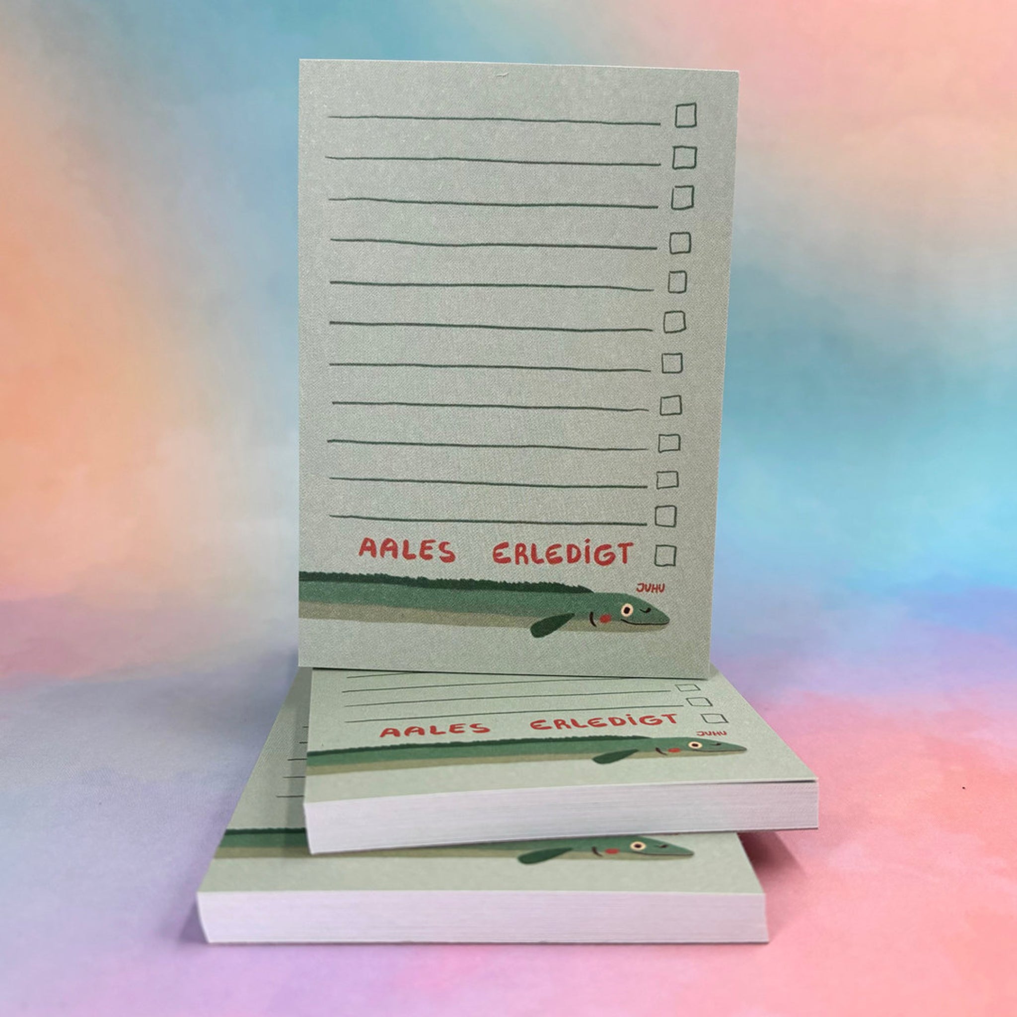 Notizblöcke mit Illustrationen eines Aals und der Aufschrift "AALES ERLEDIGT", auf einem bunten Hintergrund.