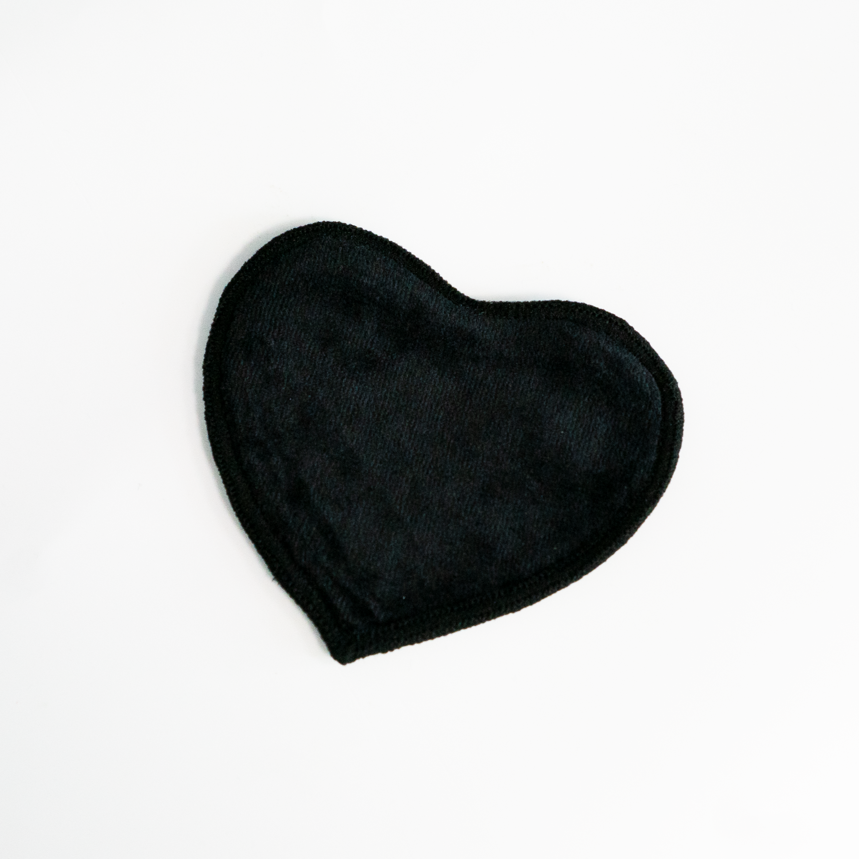 Ein schwarzes, herzförmiges Stoffstück liegt auf einer weißen Oberfläche.