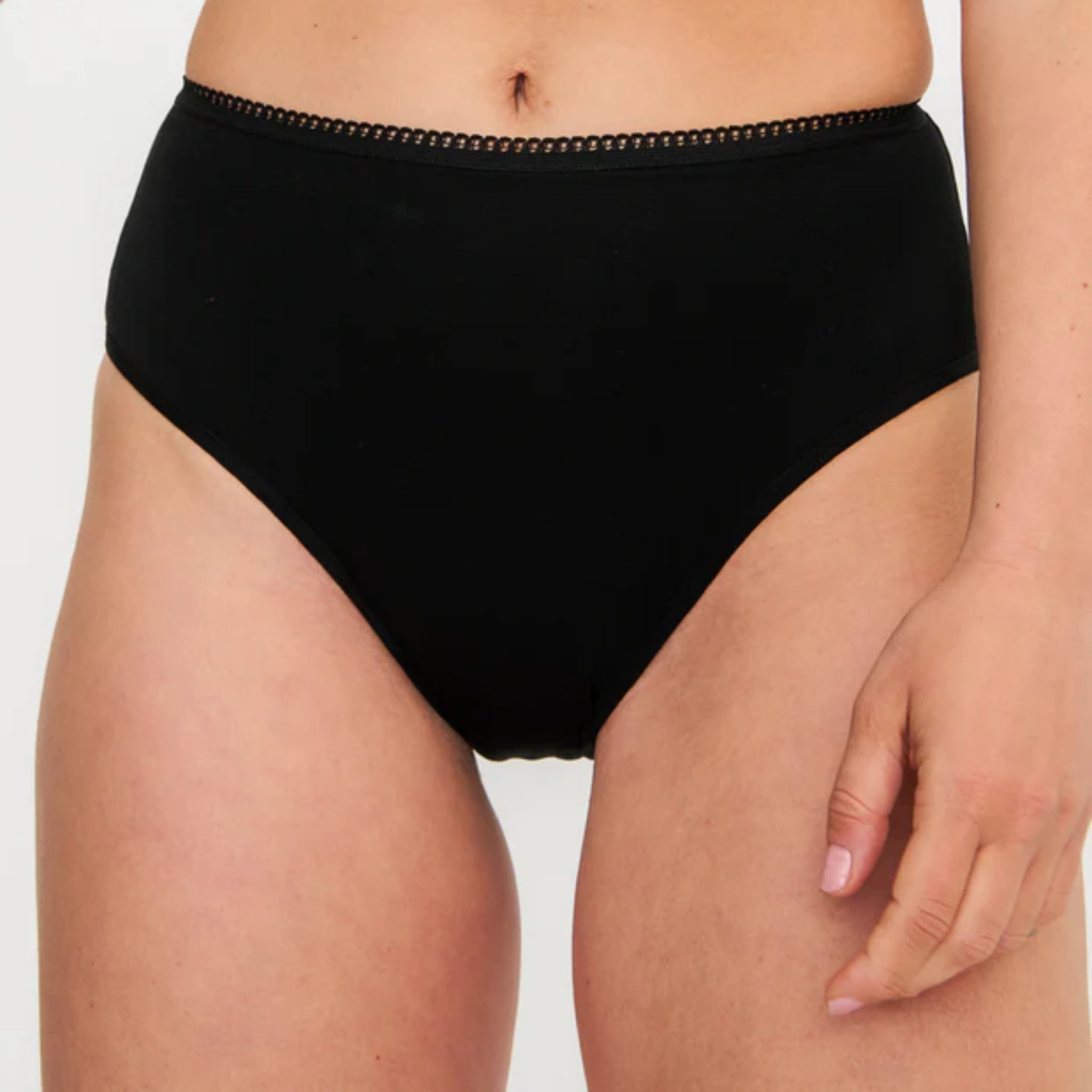 Eine Person trägt schwarze Unterwäsche mit hoher Taille und einer Zierborte am Bund, die von der Mitte des Oberkörpers bis zu den Oberschenkeln vor einem unifarbenen Hintergrund gezeigt wird.