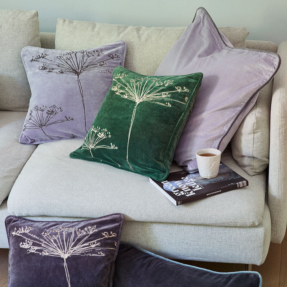 Kissen mit botanischen Motiven auf einem hellen Sofa, ein Buch und eine Tasse Kaffee liegen daneben.