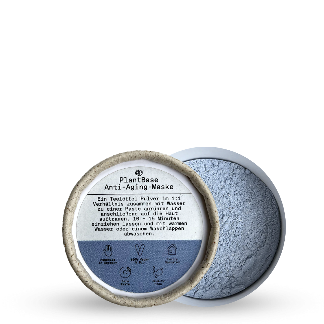 Ein geöffneter Behälter mit PlantBase Anti-Aging Mask-Pulver, mit einem blauen Pulver im Inneren und einer Anleitung in deutscher Sprache auf dem Deckel. Icons unter dem Text weisen auf vegane, grausamfreie und natürliche Produkteigenschaften hin.