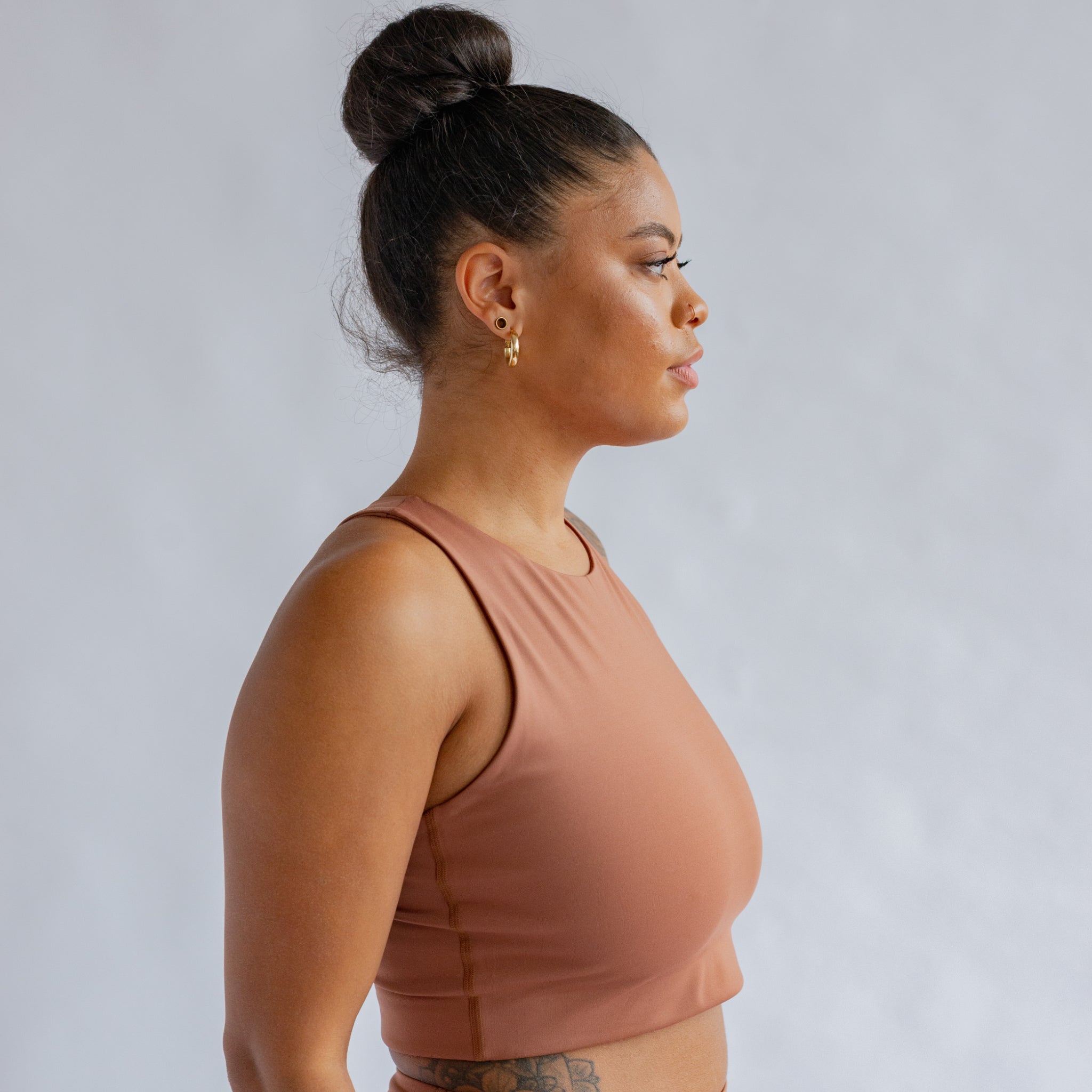 Frau im Profil mit einem Dutt und rosafarbenem Sport-Oberteil vor grauem Hintergrund.