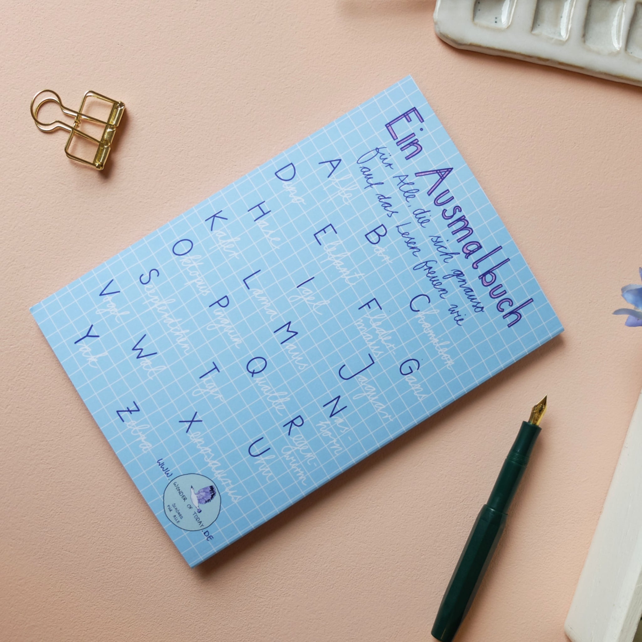 Blaues Ausmalbuch "Ein Ausmalbuch für alle, die sich gerne auf das Leben freuen" auf rosa Hintergrund mit Füller.