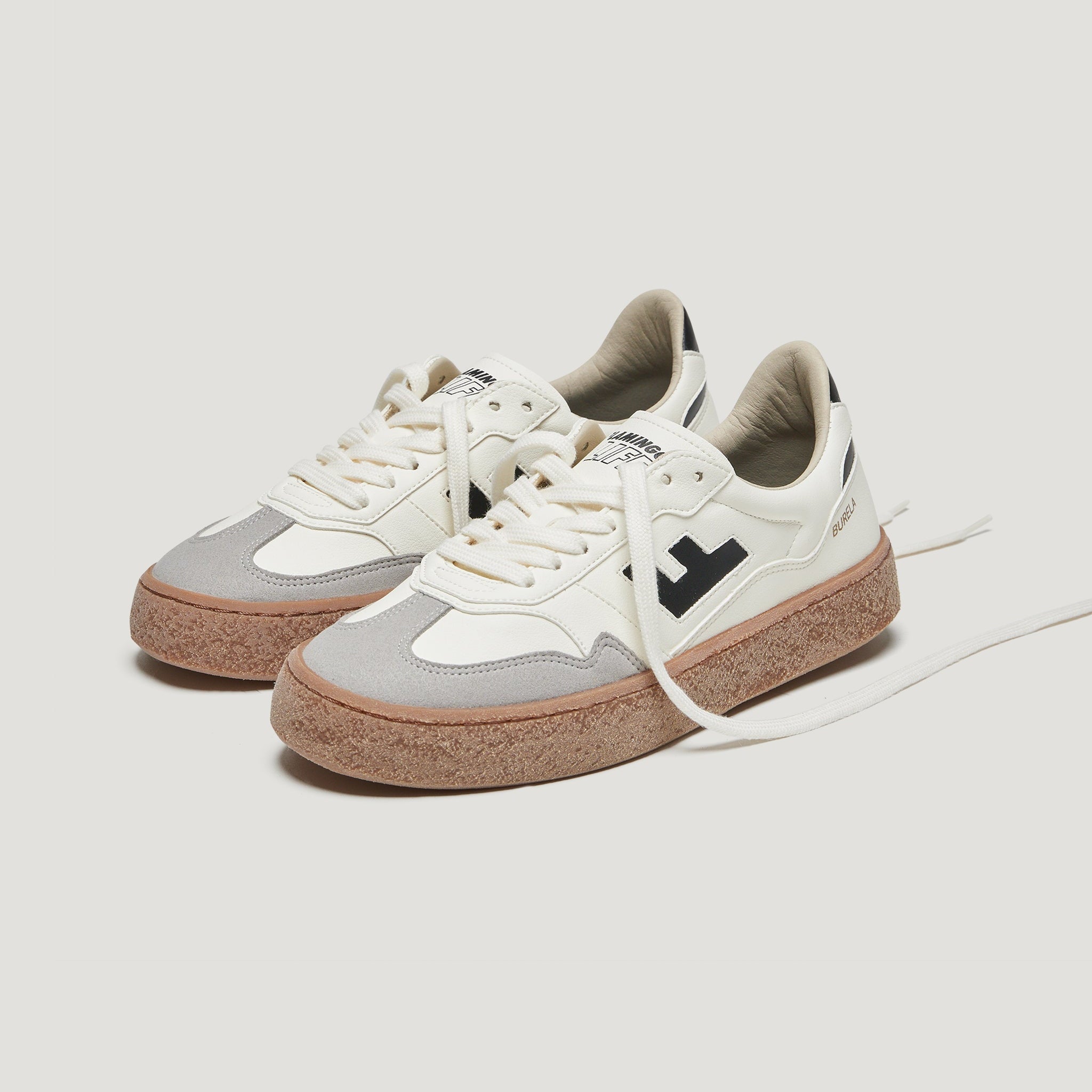 Ein Paar weiße und graue Turnschuhe mit hellbraunen, strukturierten Gummisohlen, schwarzen Akzenten und weißen Schnürsenkeln vor einem schlichten weißen Hintergrund. Der Schnürsenkel des einen Schuhs ist gelöst und liegt vorne aus.