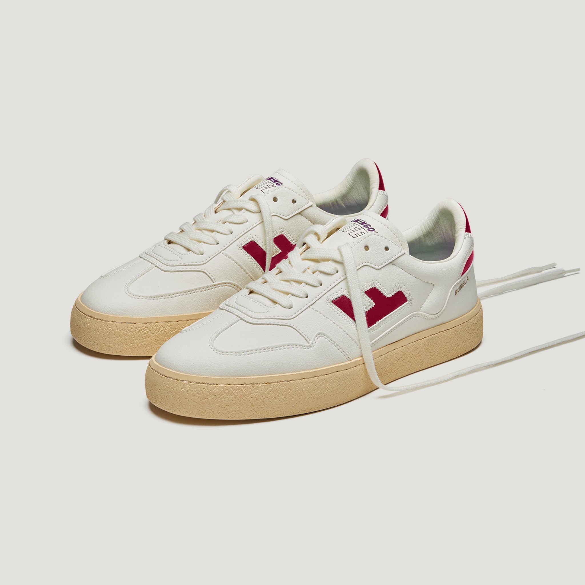 Ein Paar weiße Turnschuhe mit beiger Sohle und roten Akzenten, einschließlich eines roten Logos an den Seiten und roten Details an der Ferse, auf weißem Hintergrund.