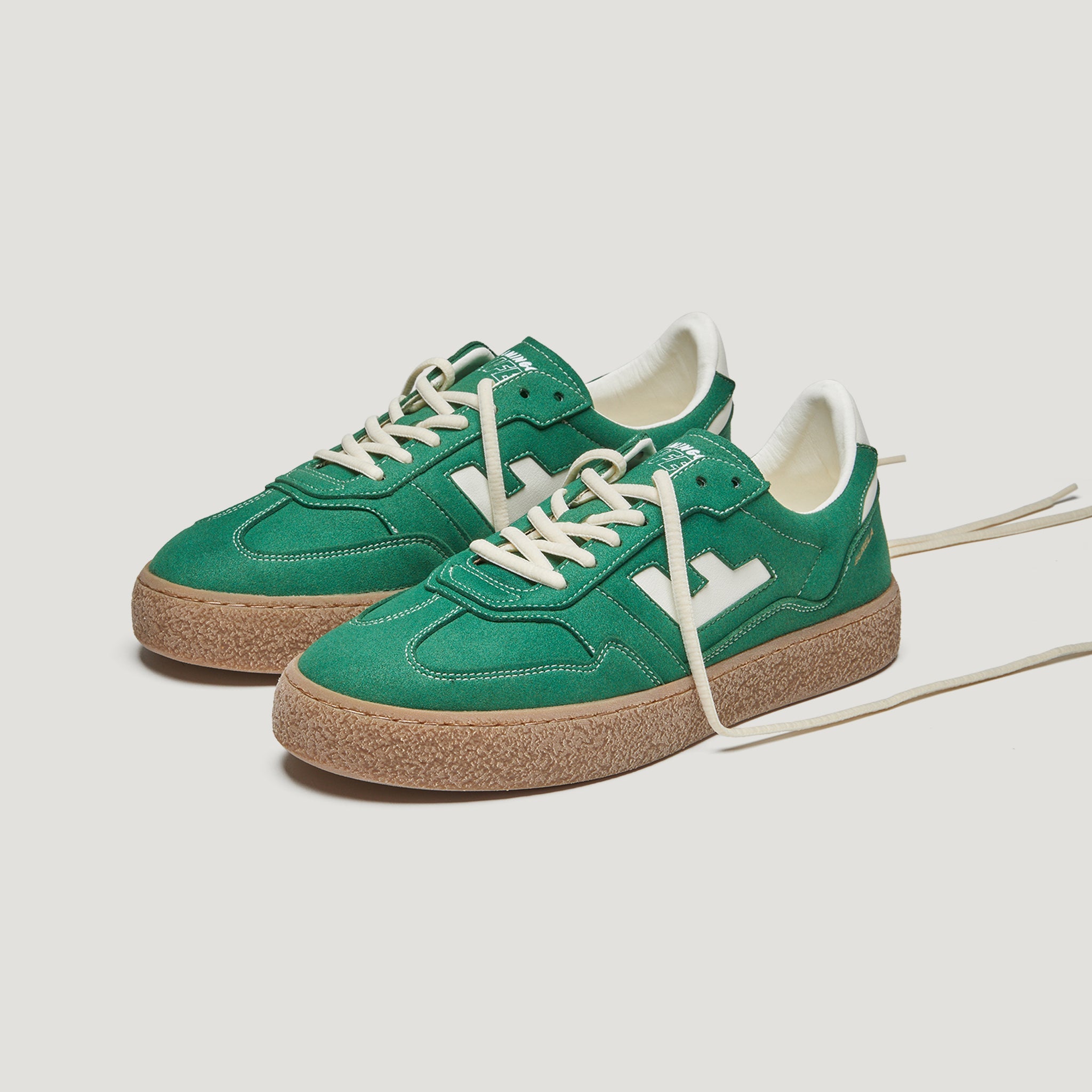 Ein Paar grüne Turnschuhe mit weißen Schnürsenkeln, weißen Akzenten und dicken braunen strukturierten Sohlen auf weißem Hintergrund.