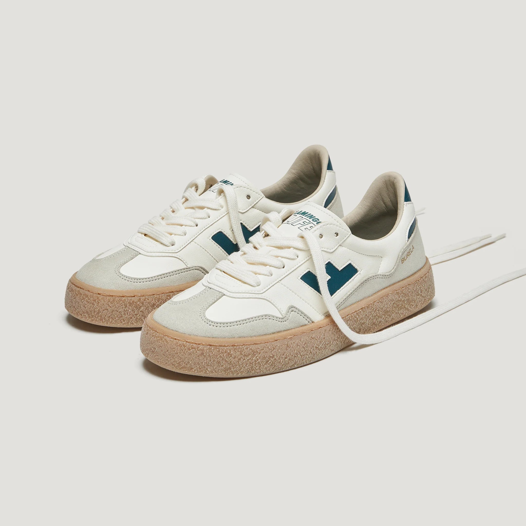Weiße Turnschuhe mit dickem braunem Sohlenrand und dunklen Akzenten auf der Seite.