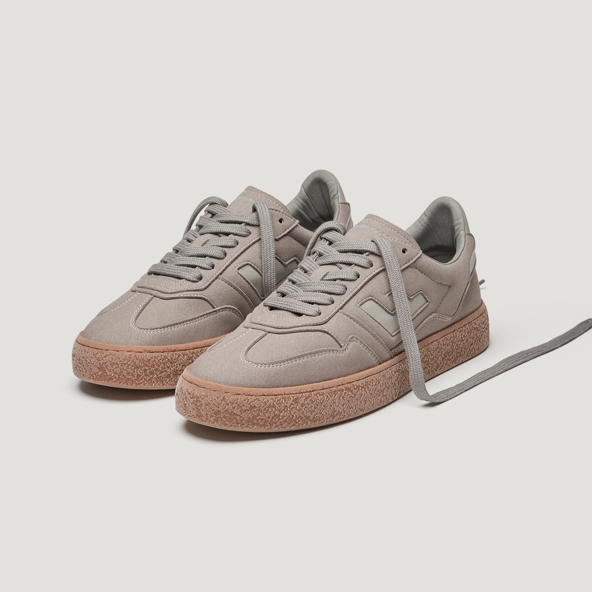 Graue Sneakers mit beiger Sohle und Schnürsenkeln auf weißem Hintergrund.