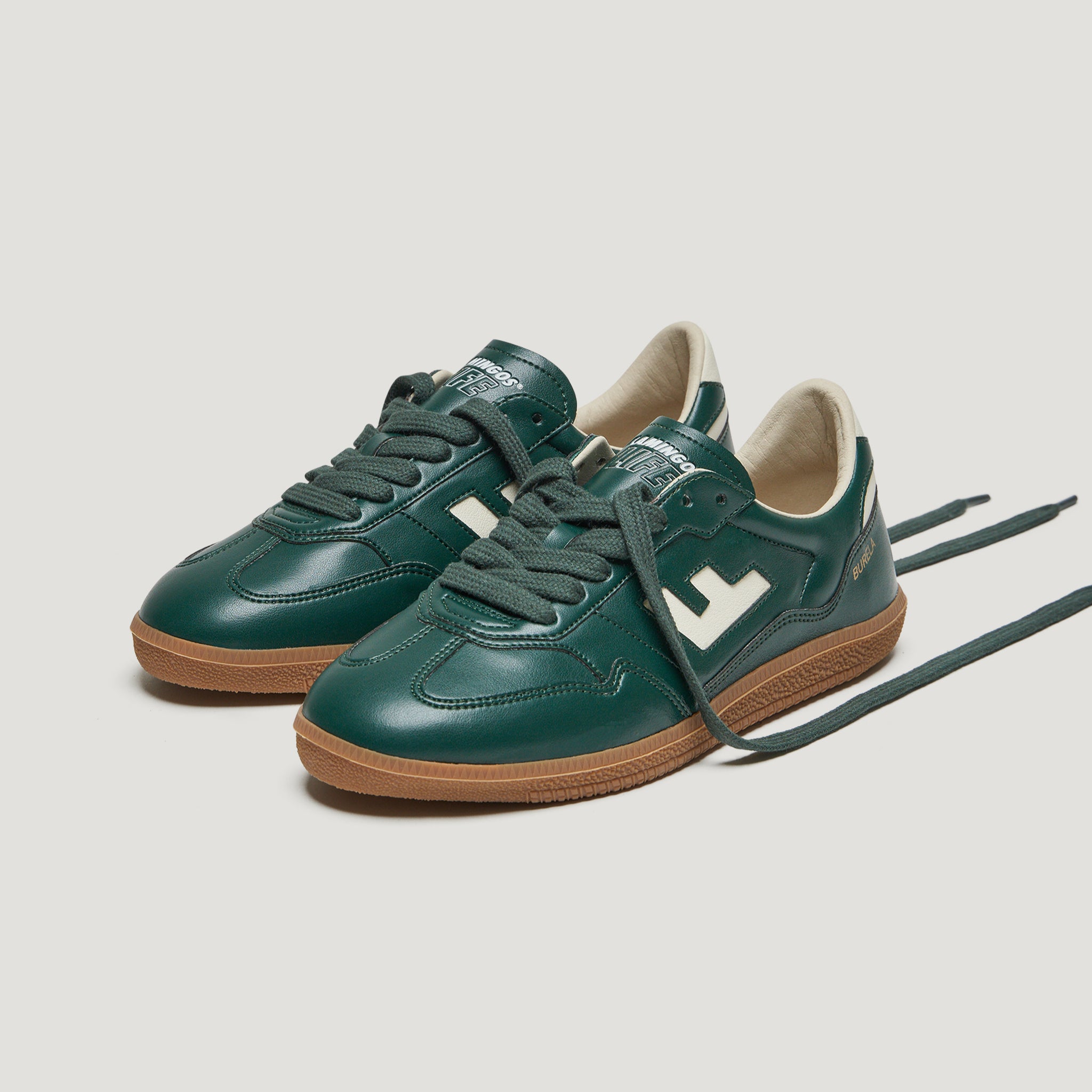 Grüne Turnschuhe mit brauner Sohle und weißen Details stehen auf einem weißen Hintergrund.