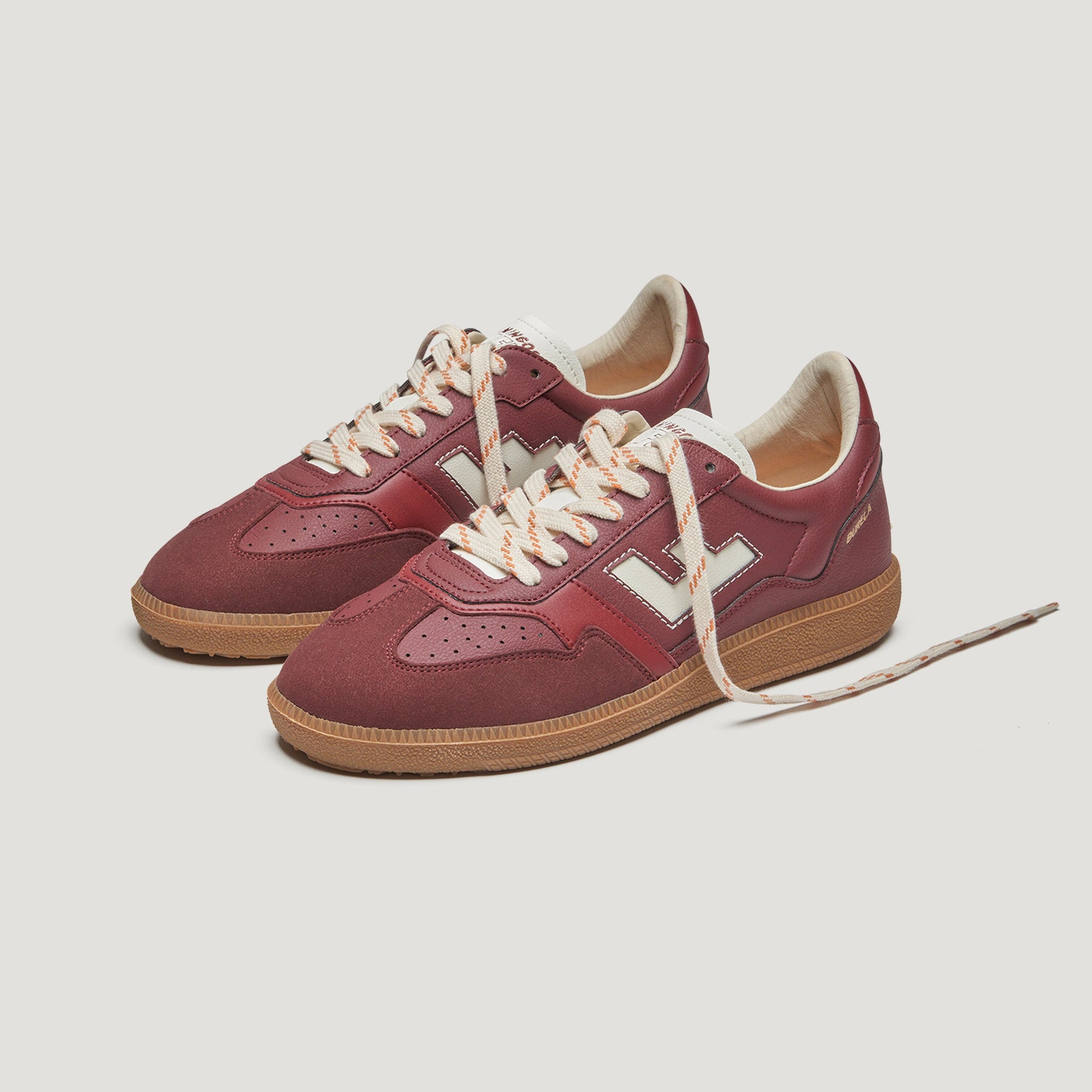 Ein Paar kastanienbraune Turnschuhe mit weißen Akzenten, beigen Sohlen, weißen V-Logos an den Seiten und beigen und kastanienbraunen Schnürsenkeln, die vor einem schlichten weißen Hintergrund stehen.